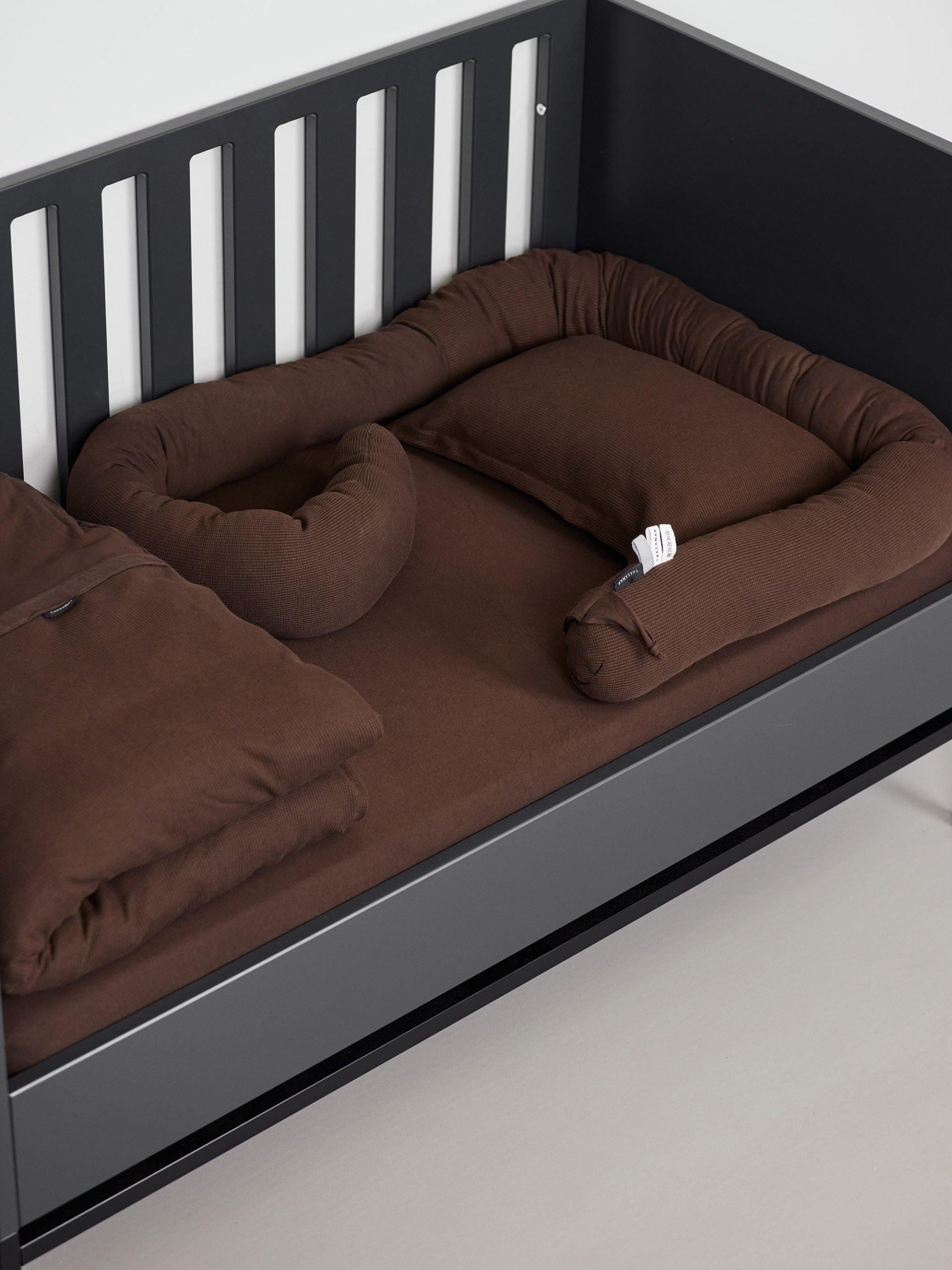 עריסת תינוק שחורה עם מצעים הכוללים סדין לתינוק, כרית נחשוש, שמיכת פוך מקופלת לתינוק וכרית עם ציפית לכרית תינוק