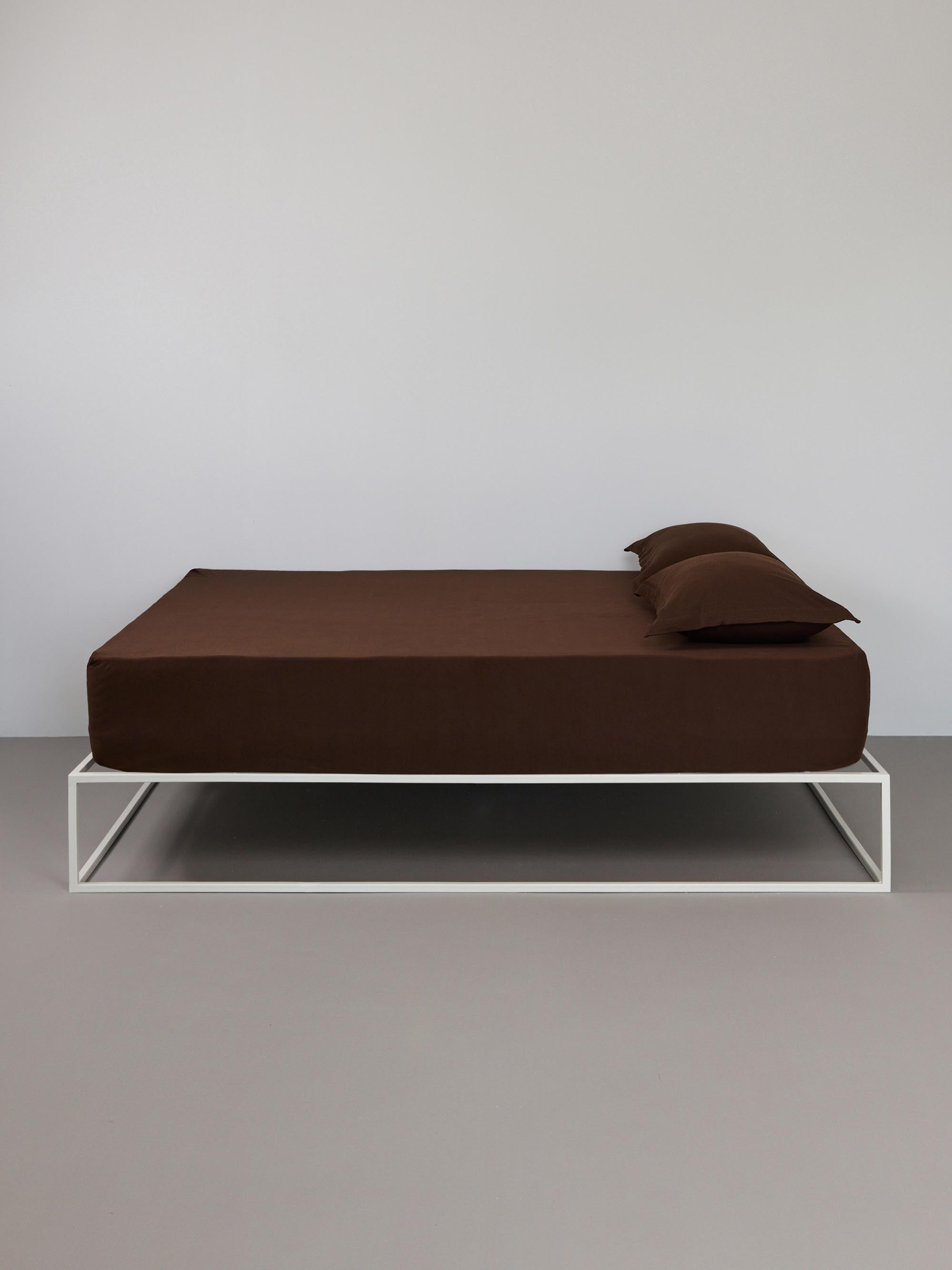 בתמונה: מיטת ברזל לבנה עם סדין וכרית עם ציפית לכרית טריקו Jacquard בצבע חום