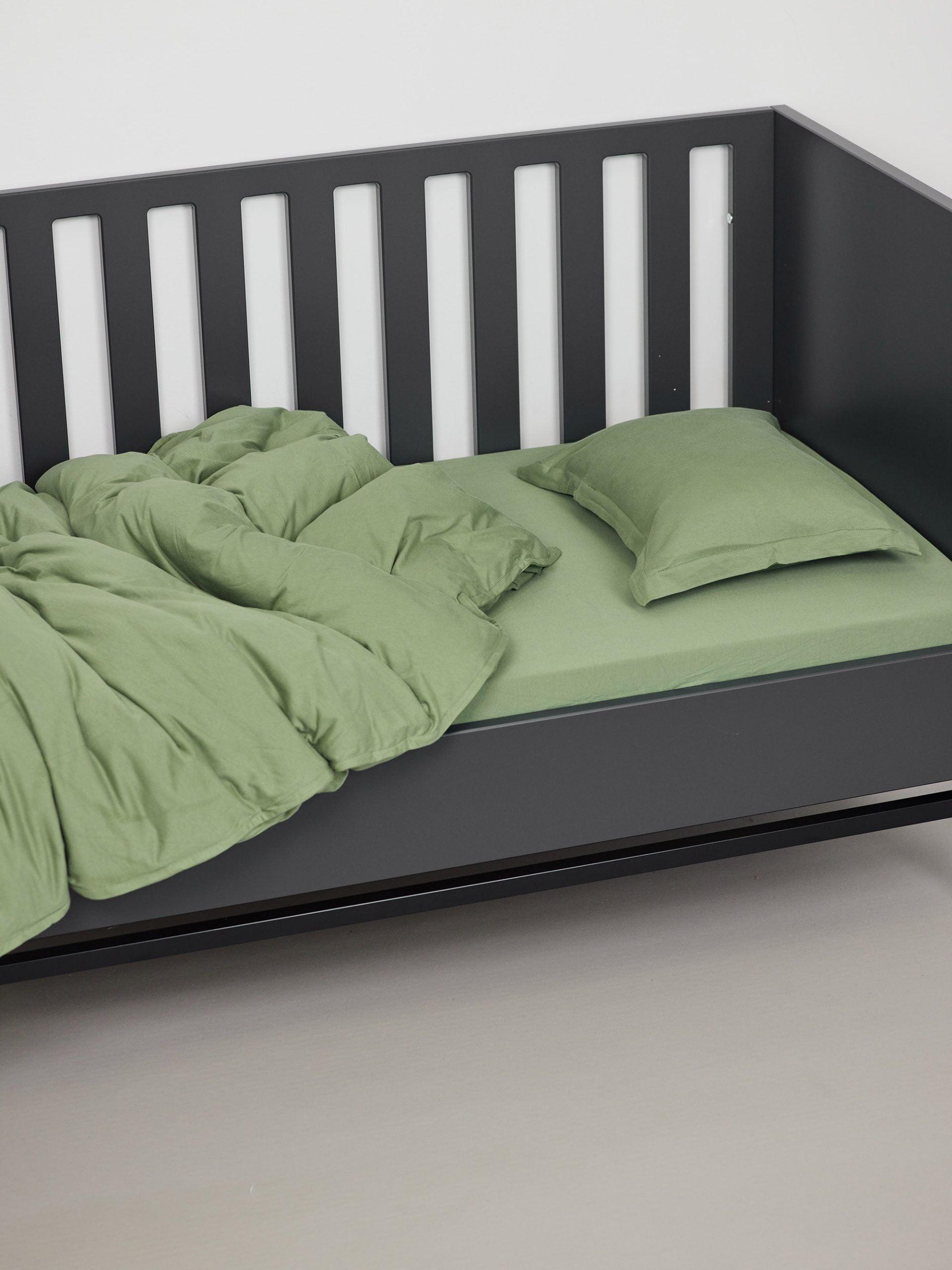 כרית עם ציפית לכרית תינוק, שמיכת פוך וסדין לתינוק בצבע ערבה בתוך עריסה שחורה