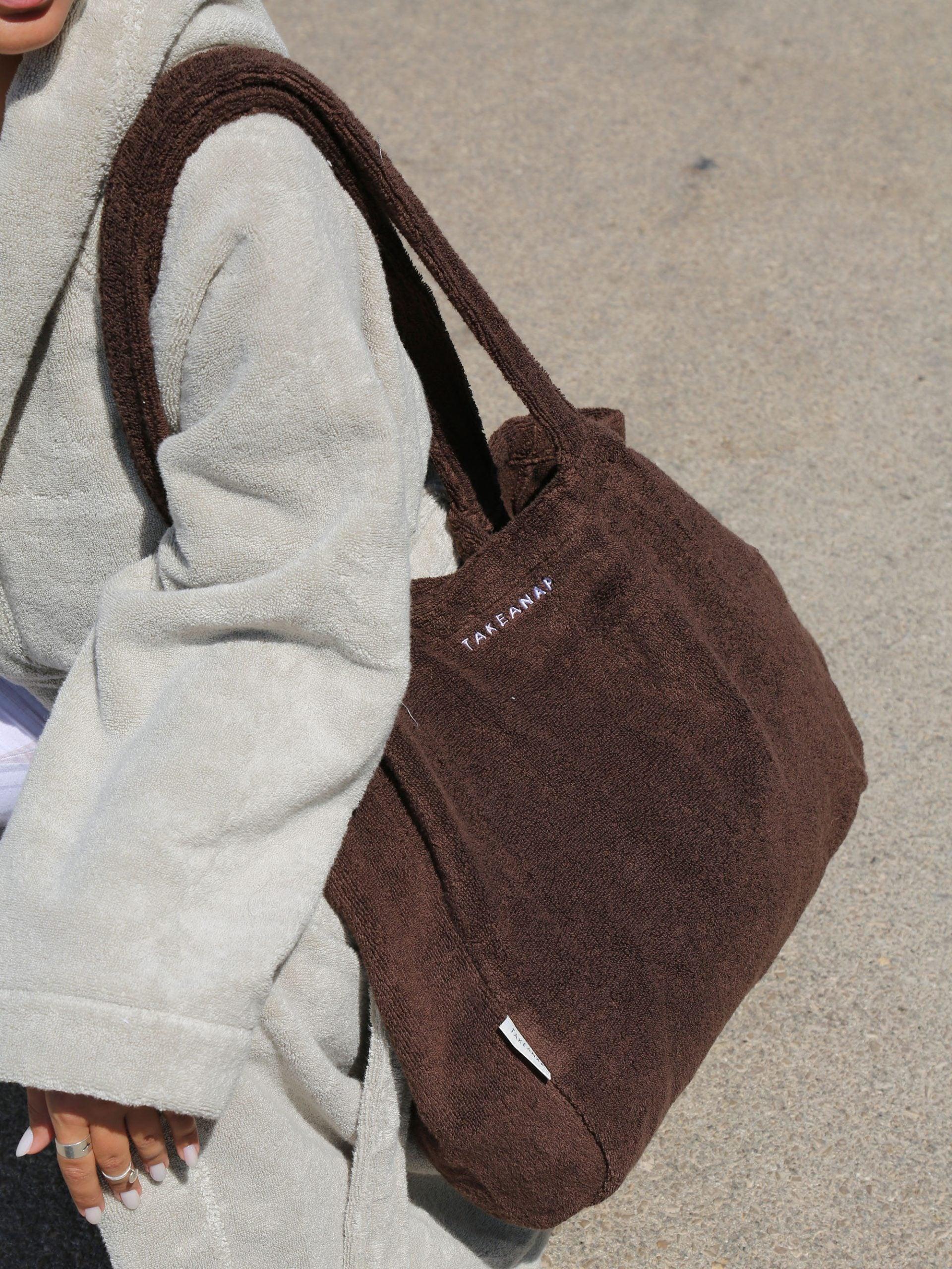 אישה לובשת חלוק ועונדת על כתפה תיק לים בצבע חום