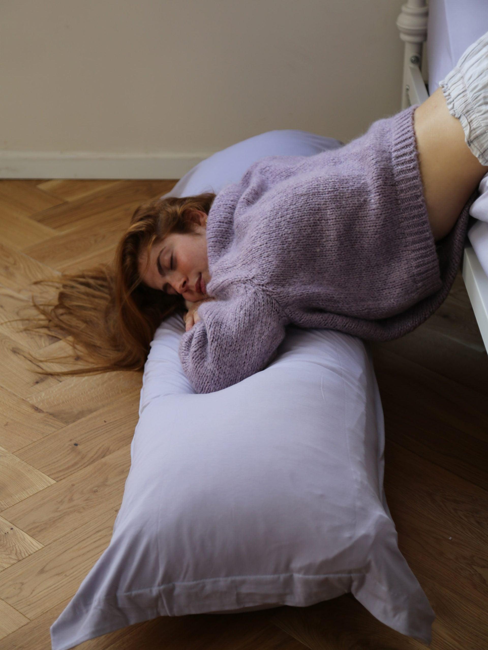 אישה מניחה את ראשה על כרית אוקספורד עם ציפית לכרית ארוכה כשהרגליים שלה על מיטת ברזל לבנה עם מצעים