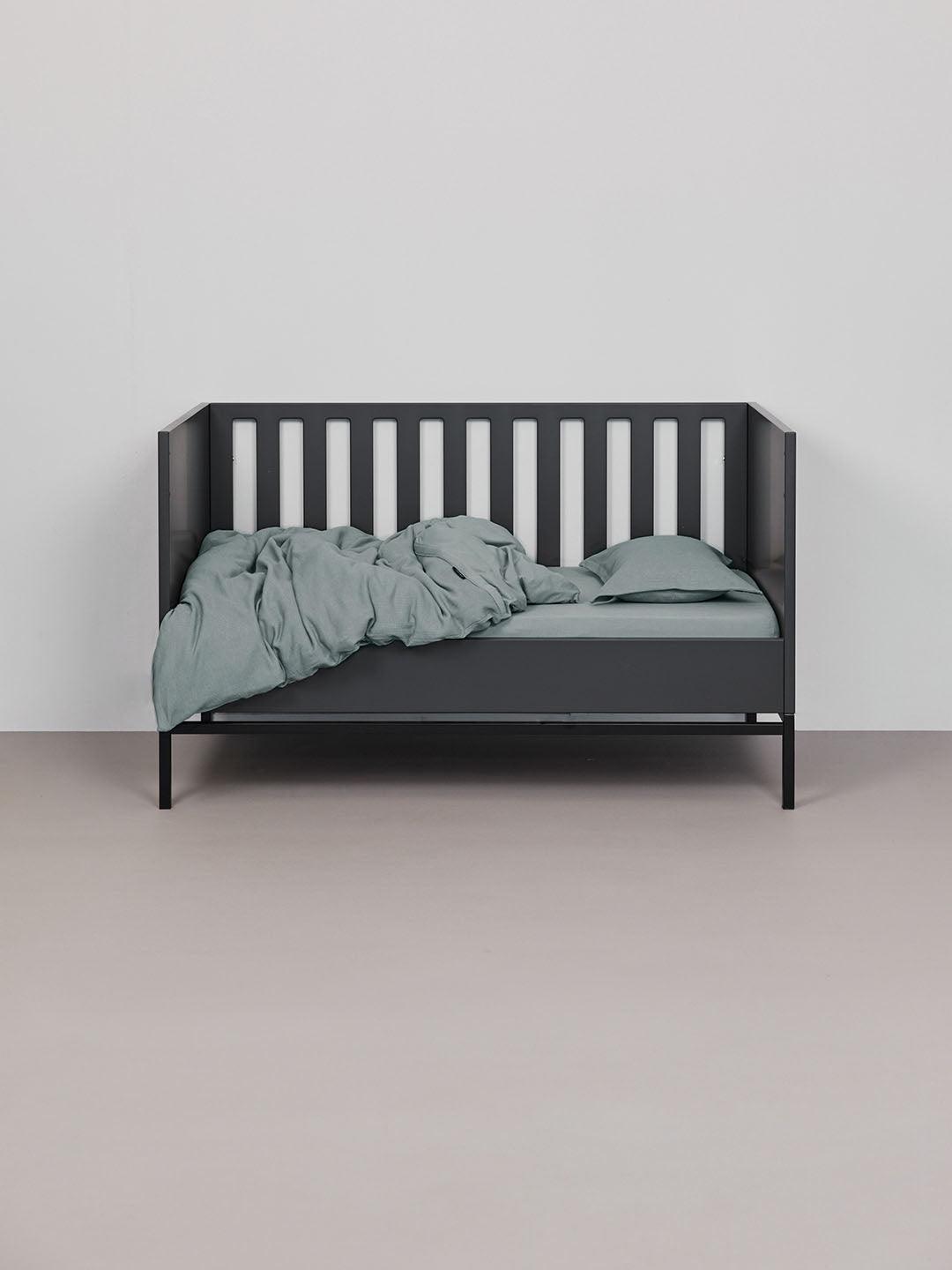 מצעים למיטת תינוק בצבע אקווה בתוך עריסה שחורה פתוחה הכולל סדין, שמיכת קיץ וכרית