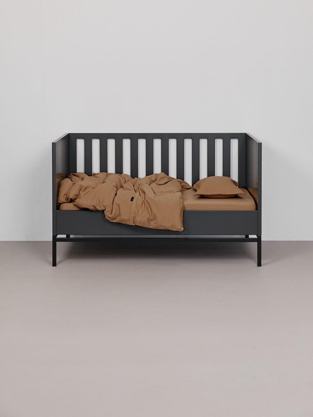 מצעים למיטת תינוק בצבע טופי בתוך עריסה שחורה פתוחה הכולל סדין, שמיכת קיץ וכרית