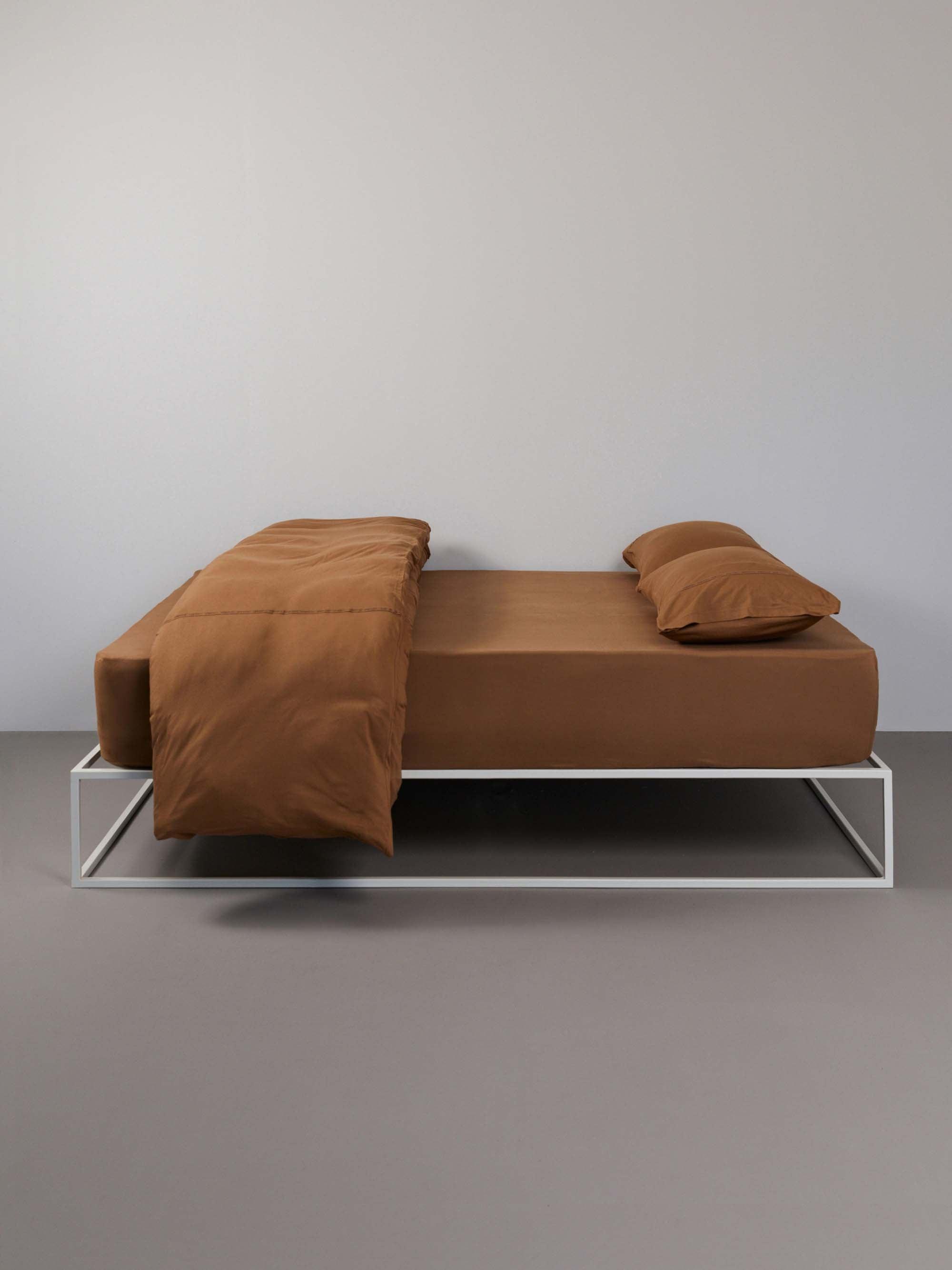 מיטת ברזל לבנה מסודרת עם סדין, שמיכה מקופלת כריות וציפיות לכריות בצבע טופי