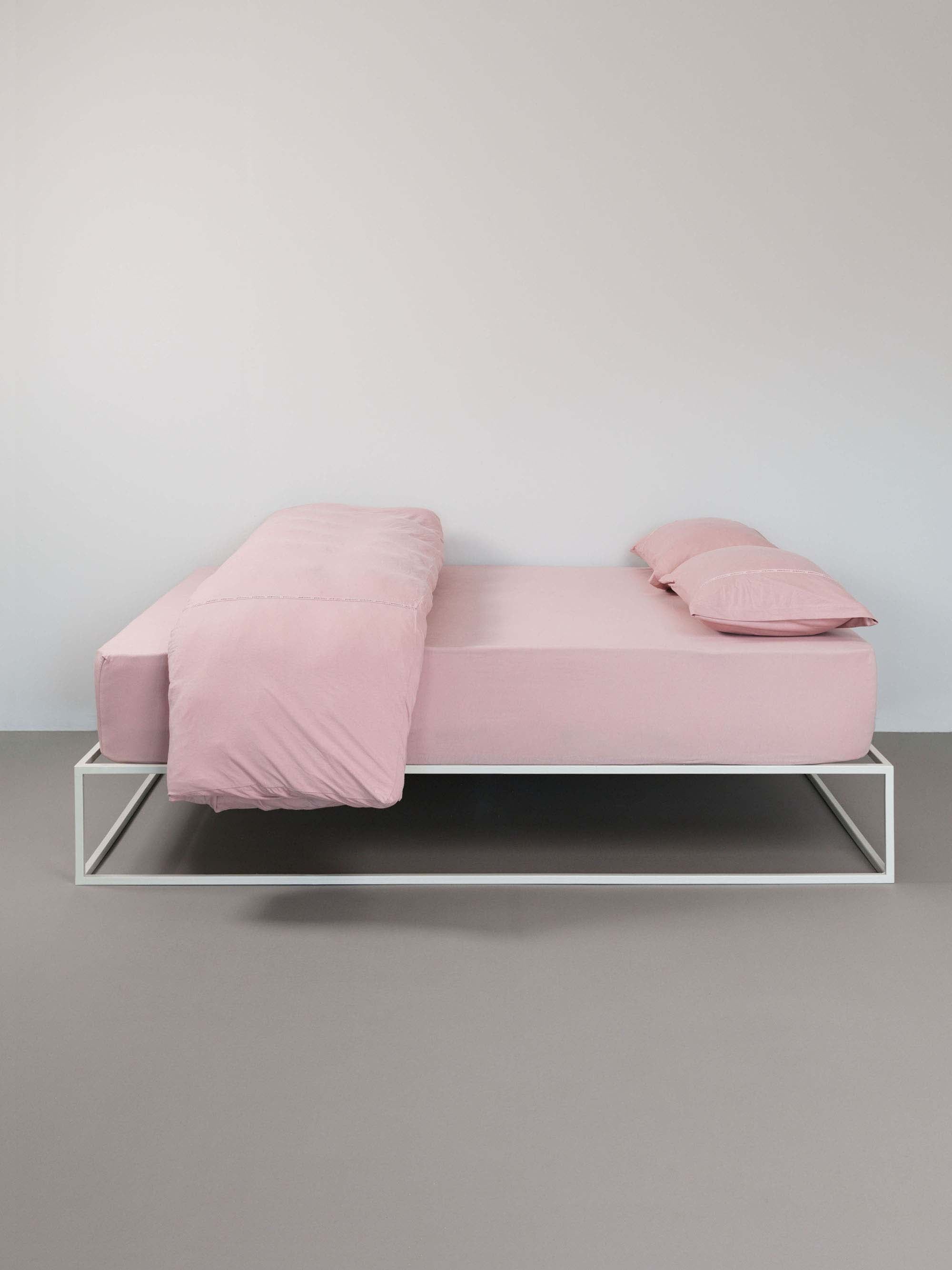 מיטת ברזל לבנה מסודרת עם סדין, שמיכה מקופלת כריות וציפיות לכריות בצבע ורוד