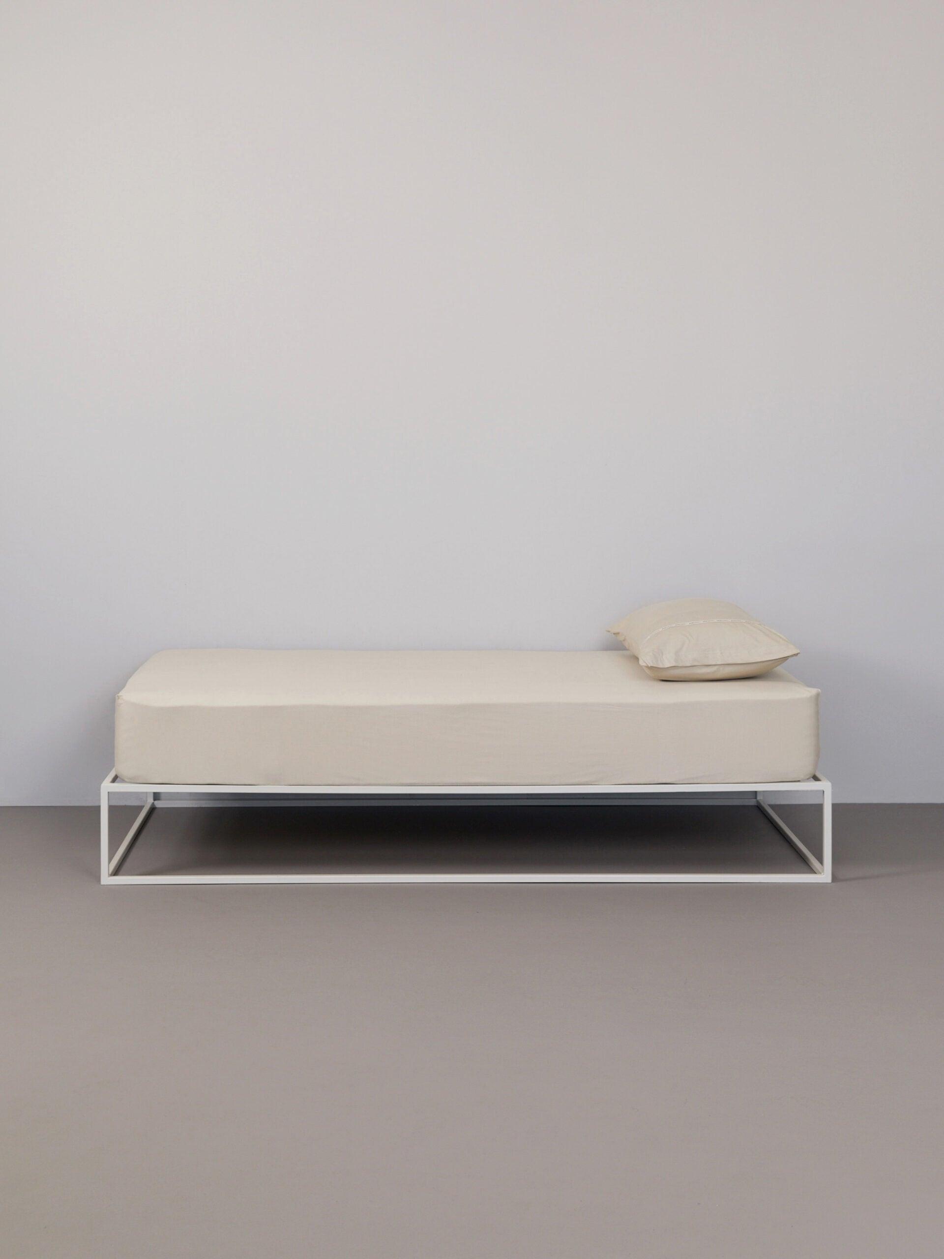 כרית עם ציפית לכרית בצבע אבן על מיטת ברזל לבנה