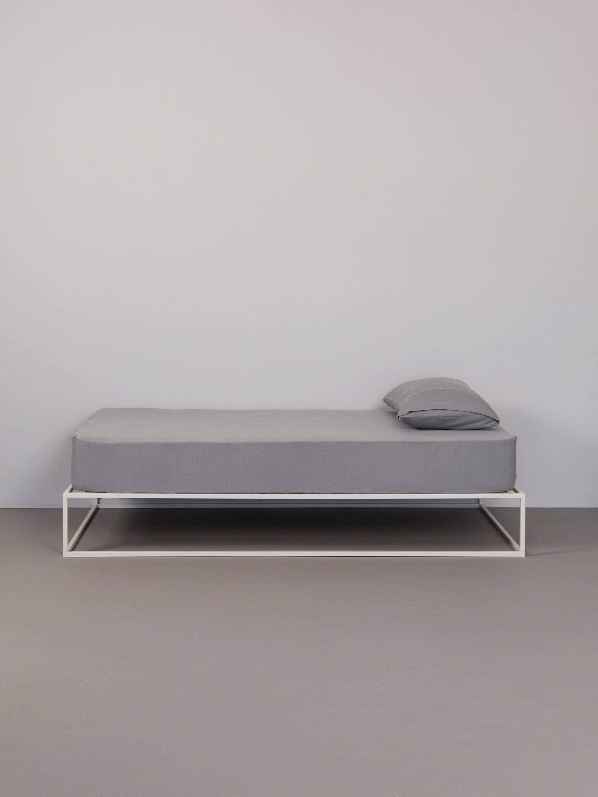 כרית עם ציפית לכרית בצבע אפור על מיטת ברזל לבנה