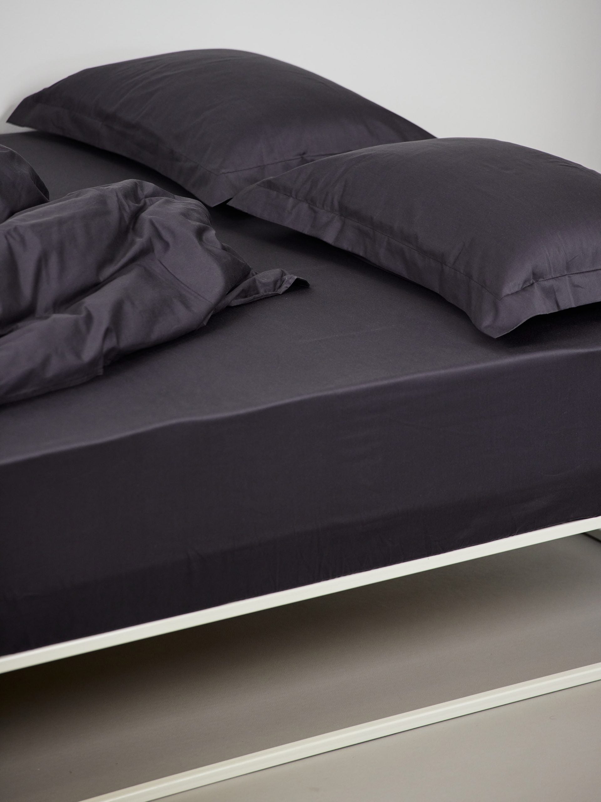מיטת ברזל לבנה עם סדין, שמיכת פוך, כריות וציפיות לכריות בצבע פחם