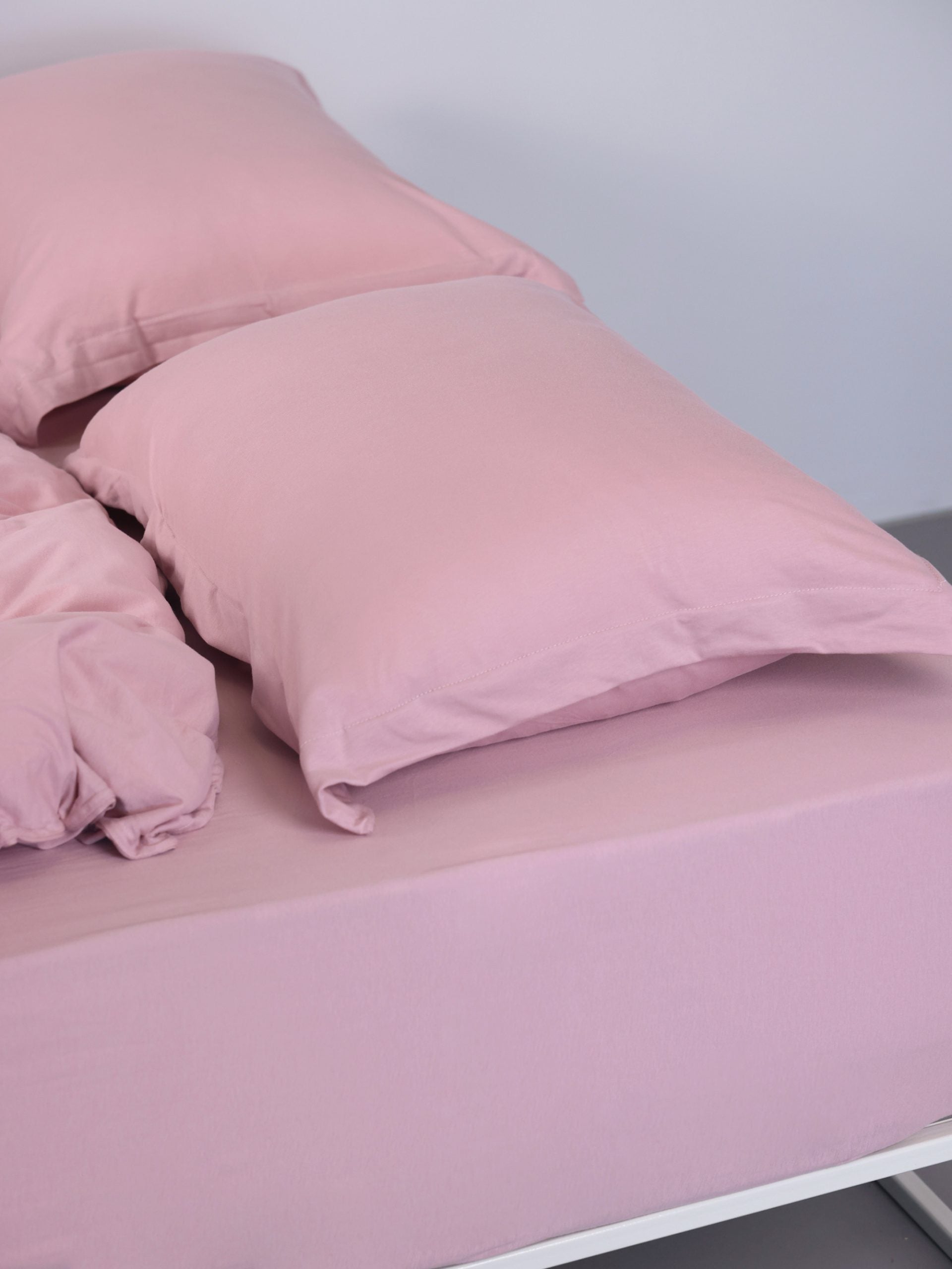 ראש מיטת ברזל לבנה עם סט מצעים וכריות עם ציפיות לכריות בצבע ורוד