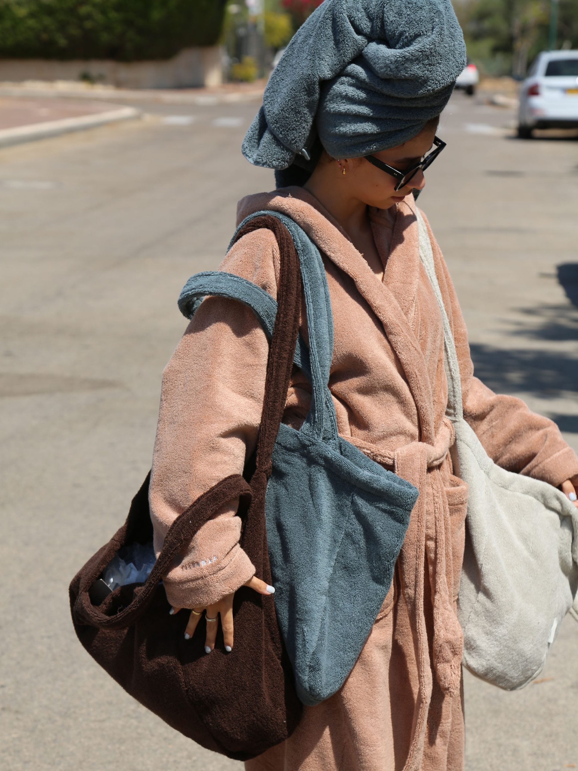 אישה לבושה בחלוק עם מגבת על הראש עונדת 3 תיקים לים 