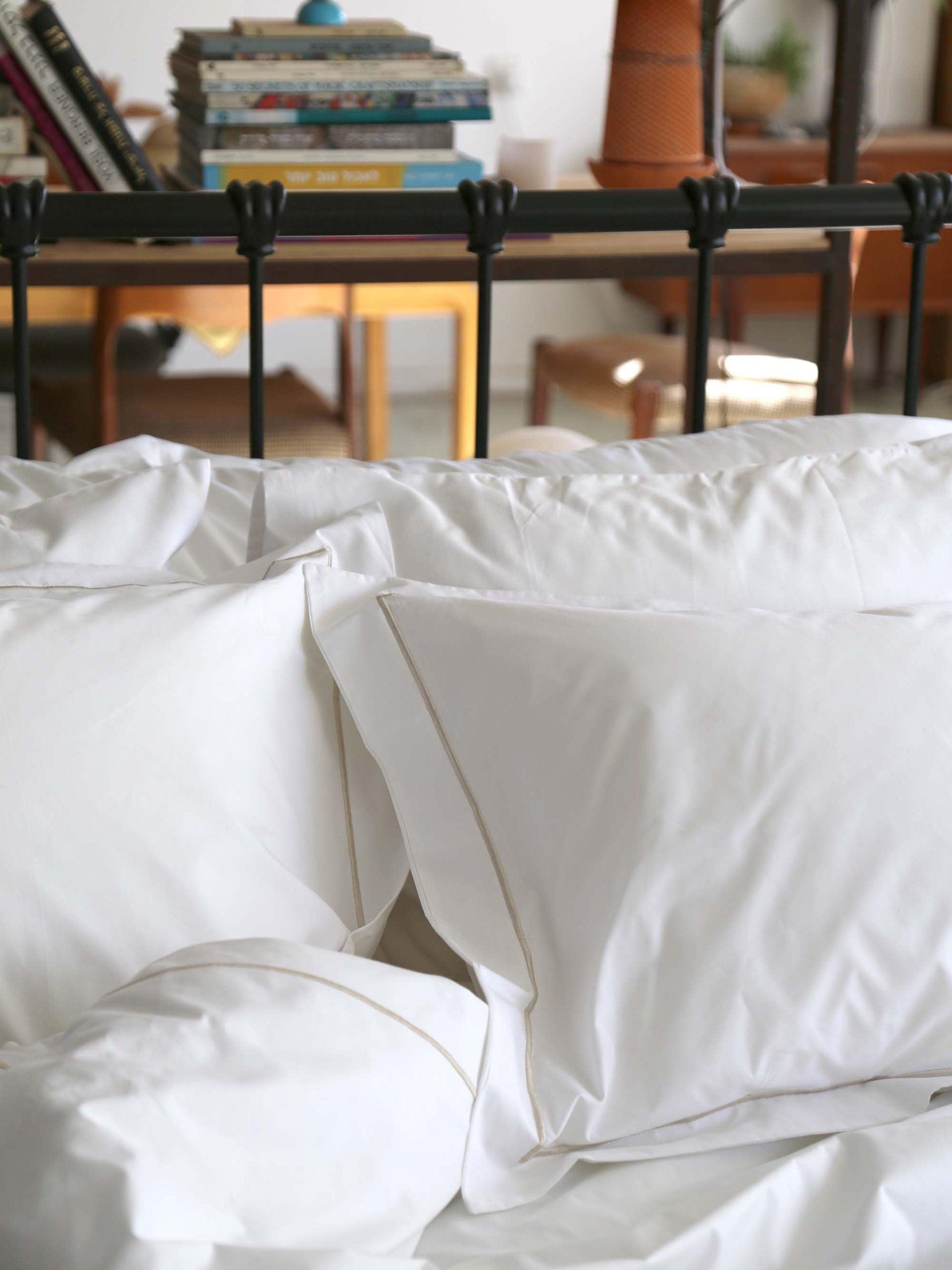 גב מיטת בכרזל שחורה שעליה מונחים ציפה לשמיכה וסט כריות לבנות עם ציפיות