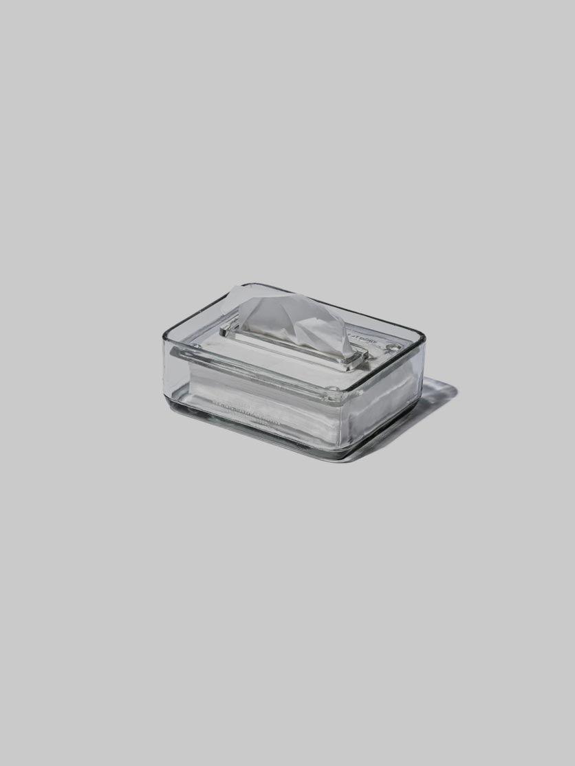 קופסת טישו מזכוכית עם נייר טישו על רקע אפור