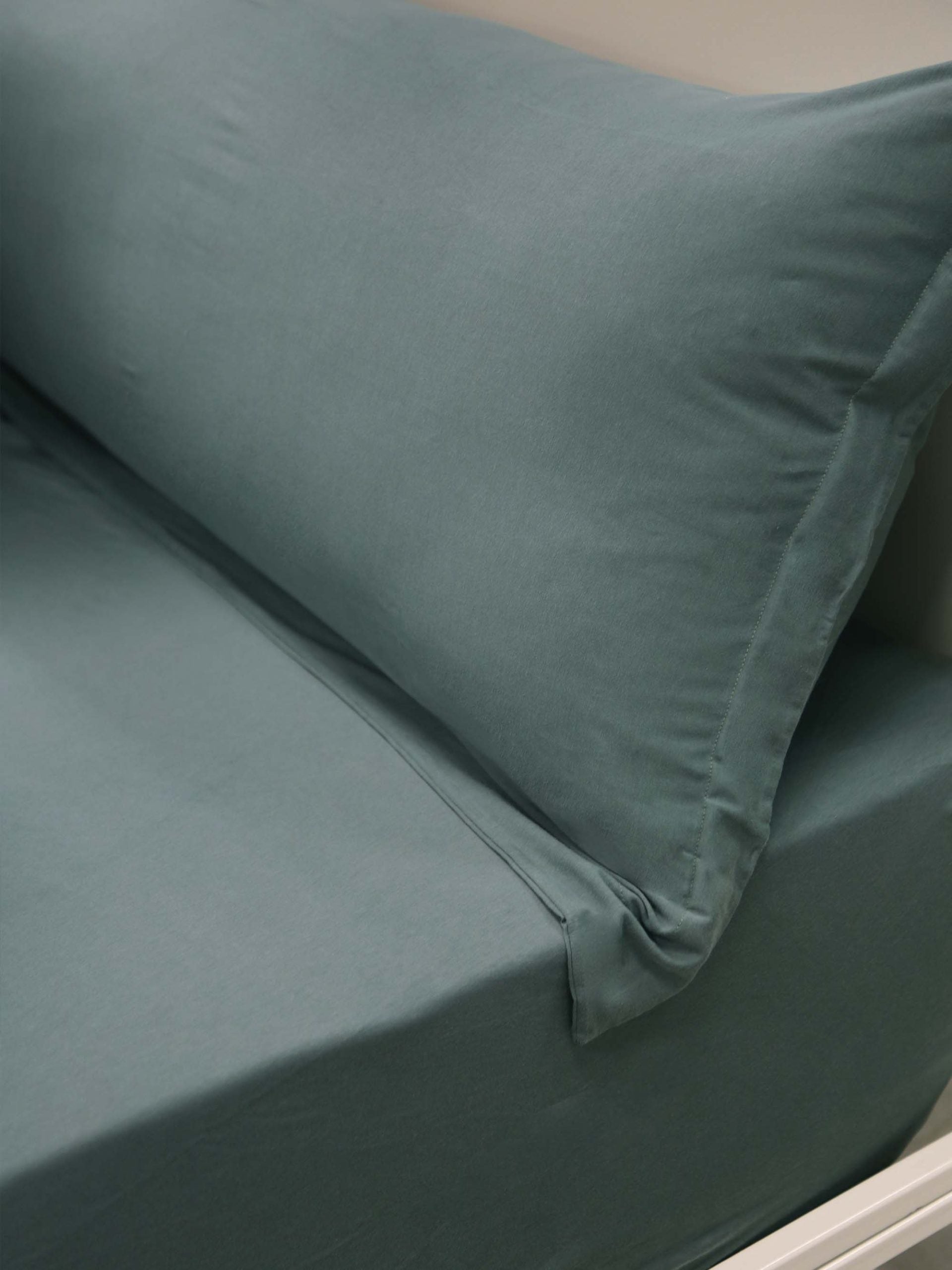 מיטת ברזל לבנה עם סדין, כרית וציפית לכרית ארוכה בצבע אושן בחדר עם קירות אפורים