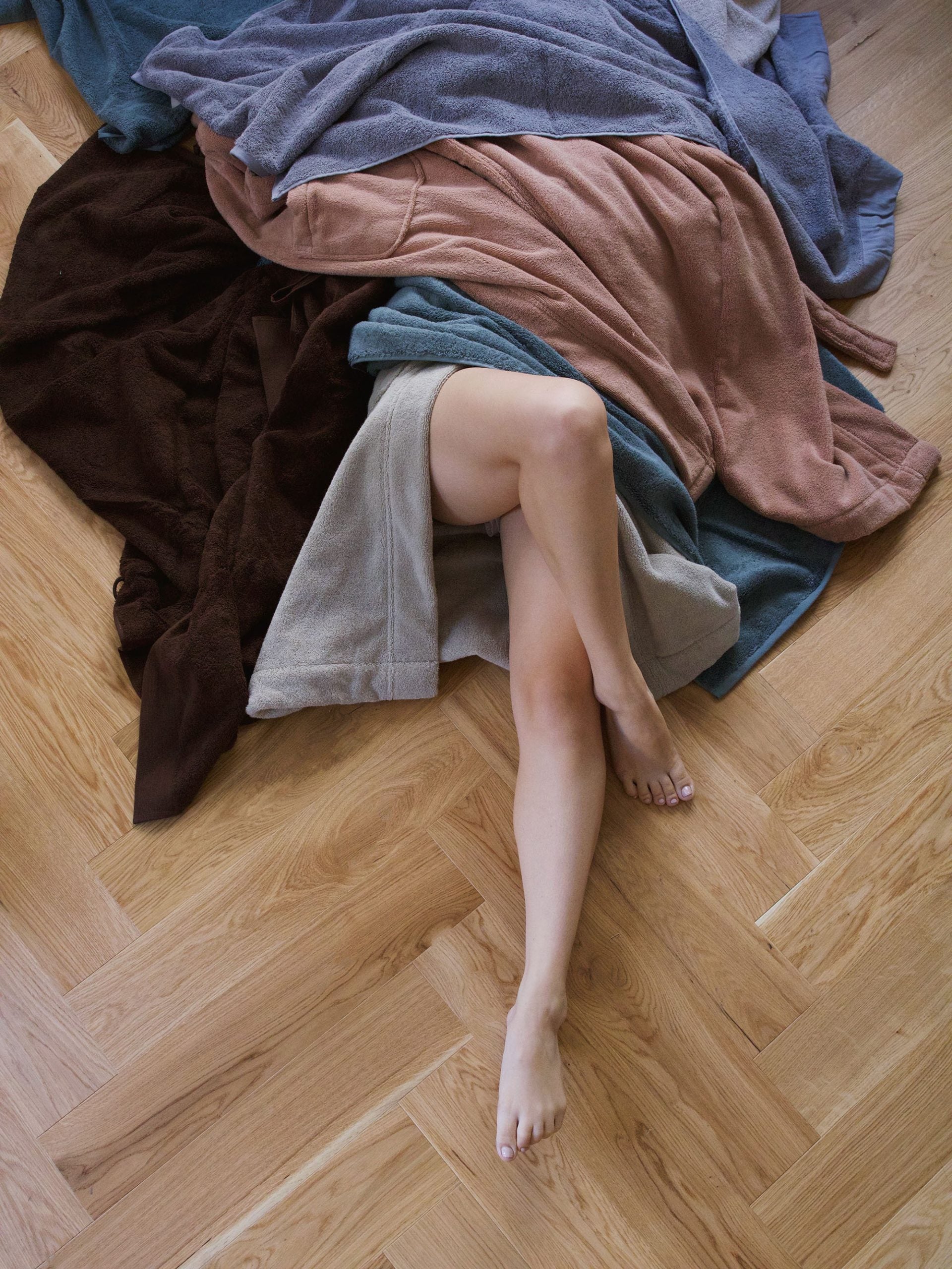 אישה  על רצפת פרקט באור יום מסתתרת מתחת למגוון חלוקי רחצה בגוונים שונים
