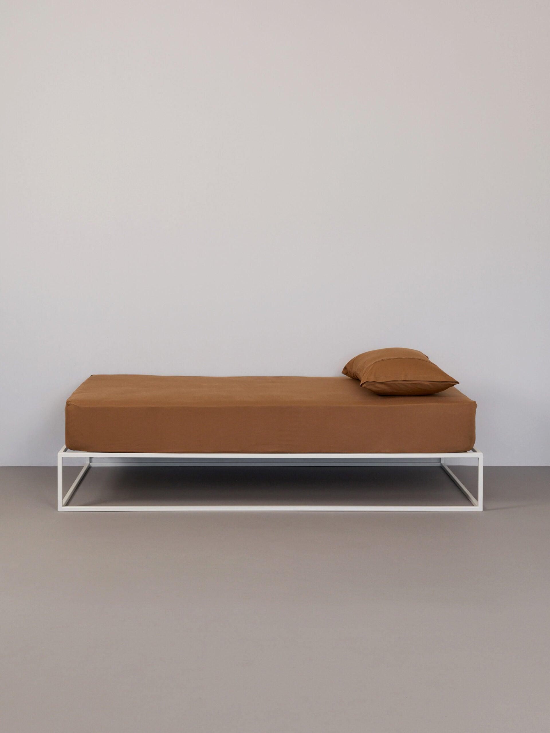 בתמונה: מיטת ברזל לבנה עם סדין וכרית עם ציפית לכרית טריקו Jacquard בצבע טבאקו