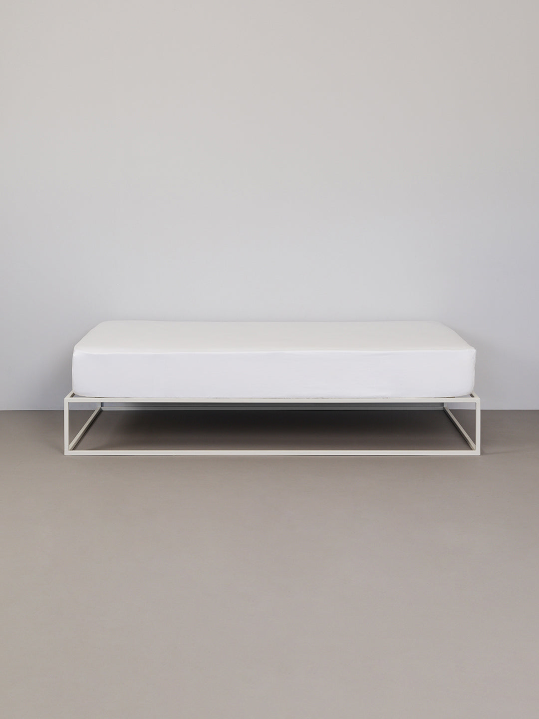 מיטת ברזל לבנה עם סדין לבן בחדר אפור בהיר בוהק