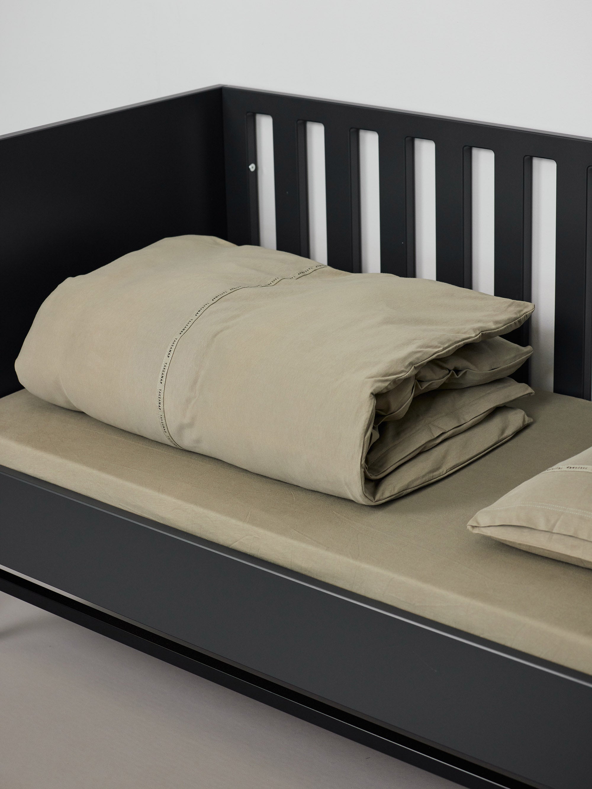 שמיכה מקופלת, סדין וכרית בתוך מיטת תינוק שחורה בצבע ירוק זית