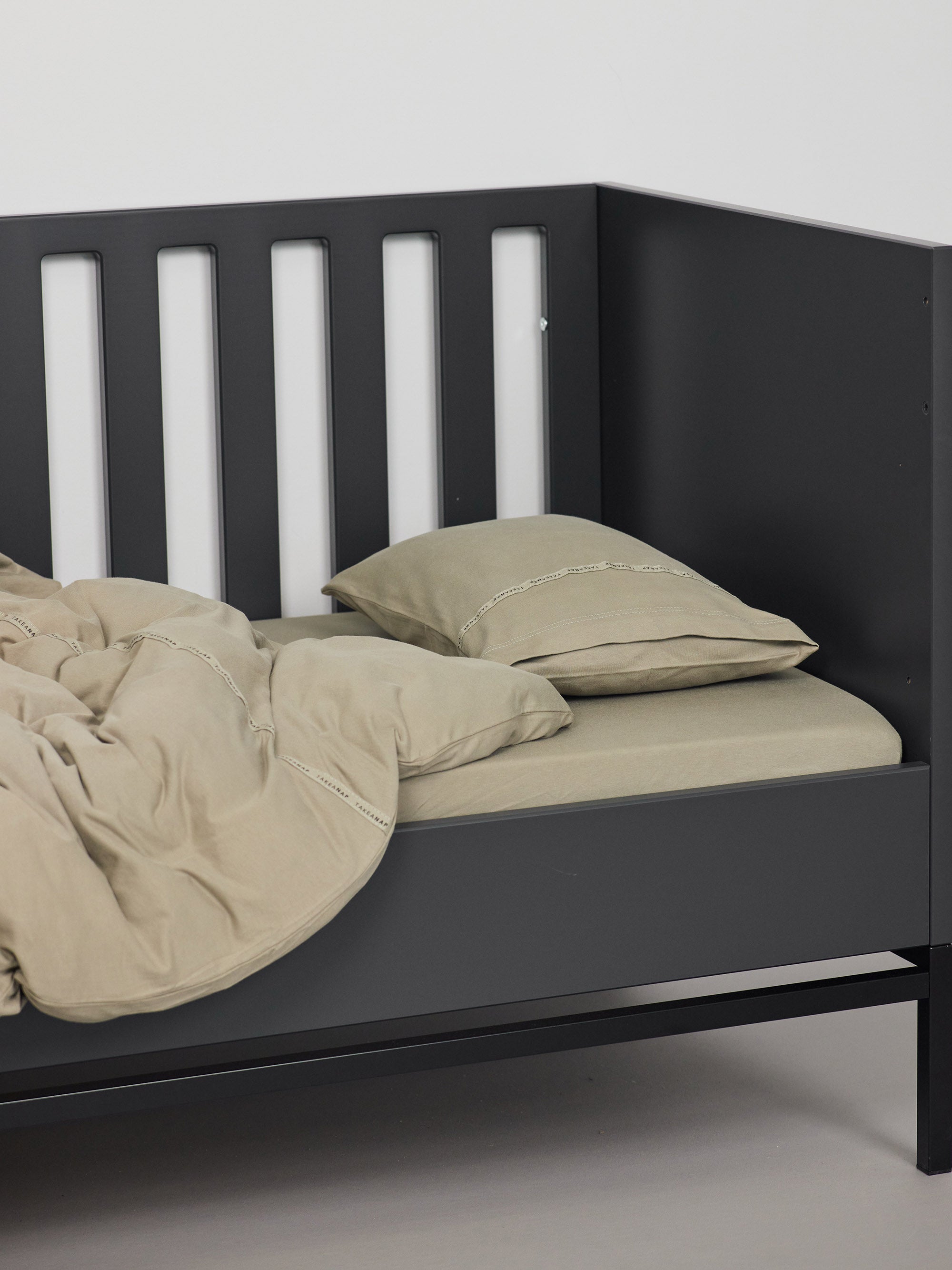 כרית עם ציפית לכרית קטנה בצבע זית עם שמיכת פוך בתוך מיטת תינוק שחורה