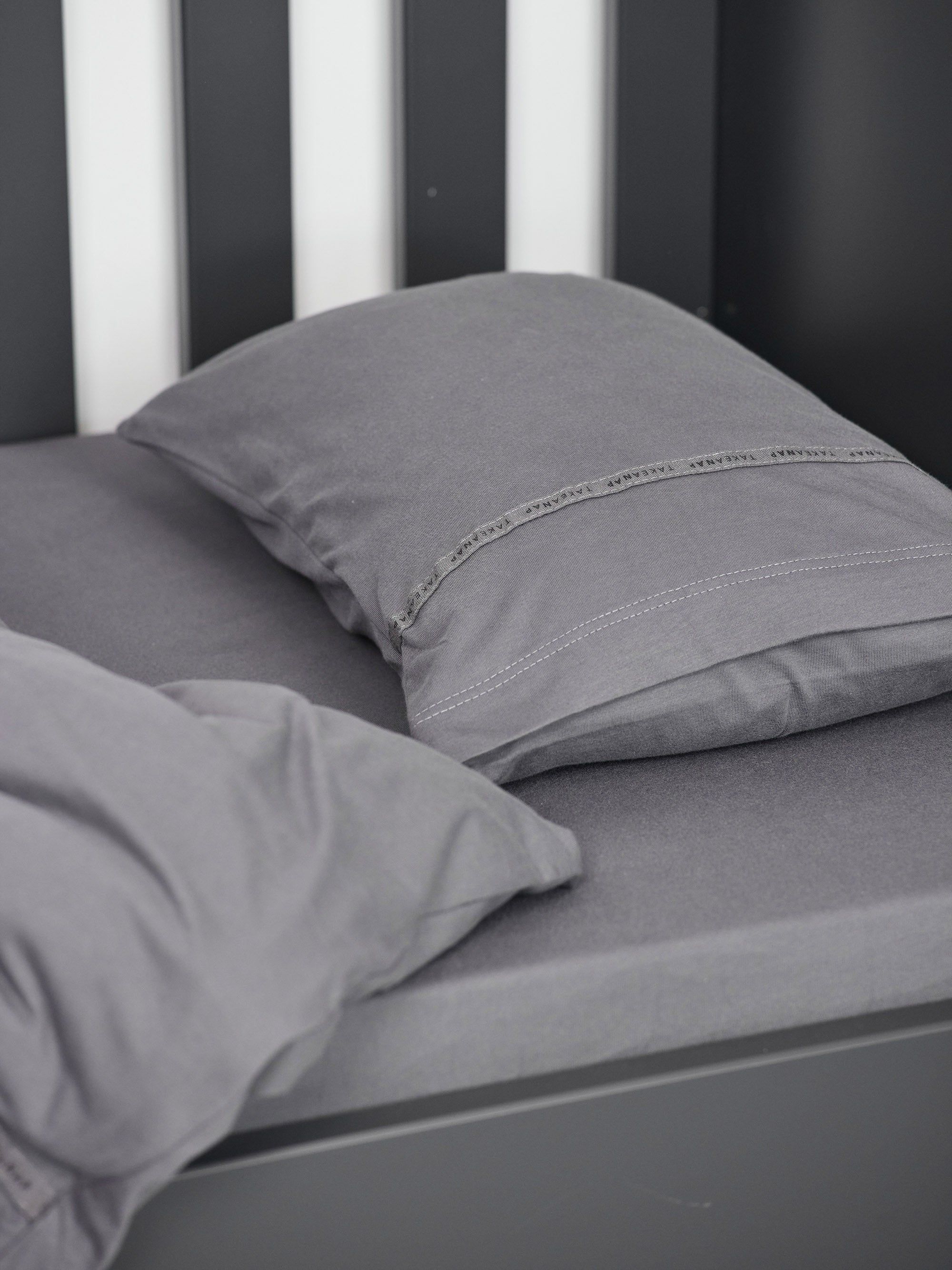 כרית עם ציפית לכרית קטנה בצבע אפור עם שמיכת פוך בתוך מיטת תינוק שחורה