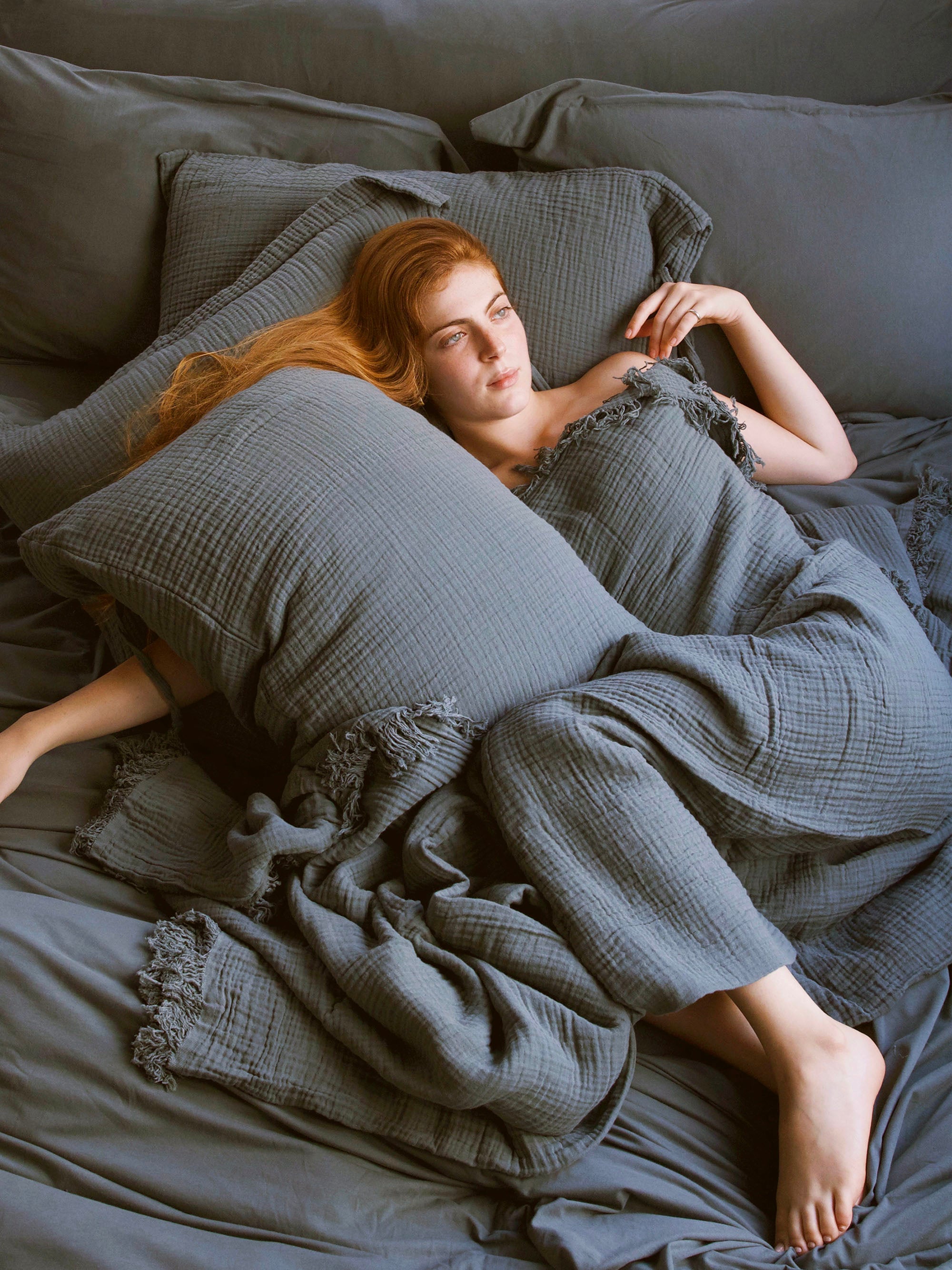 אישה מכוסה בשמיכה שוכבת על מיטה שלידה כרית עם ציפית לכרית בצבע אוושן 