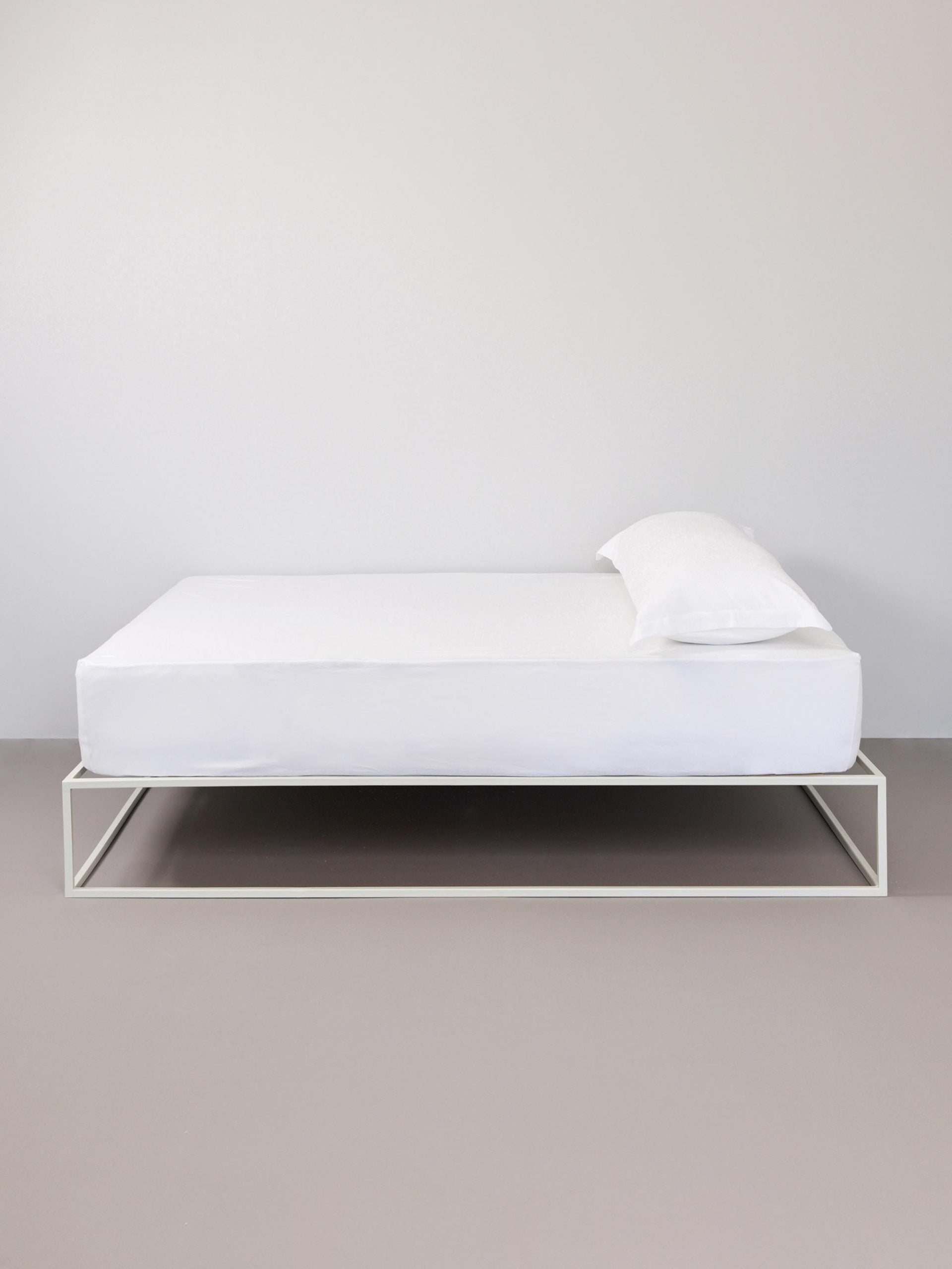 מיטת ברזל לבנה עם סדין, כרית וציפית לכרית ארוכה בצבע לבן בחדר עם קירות אפורים