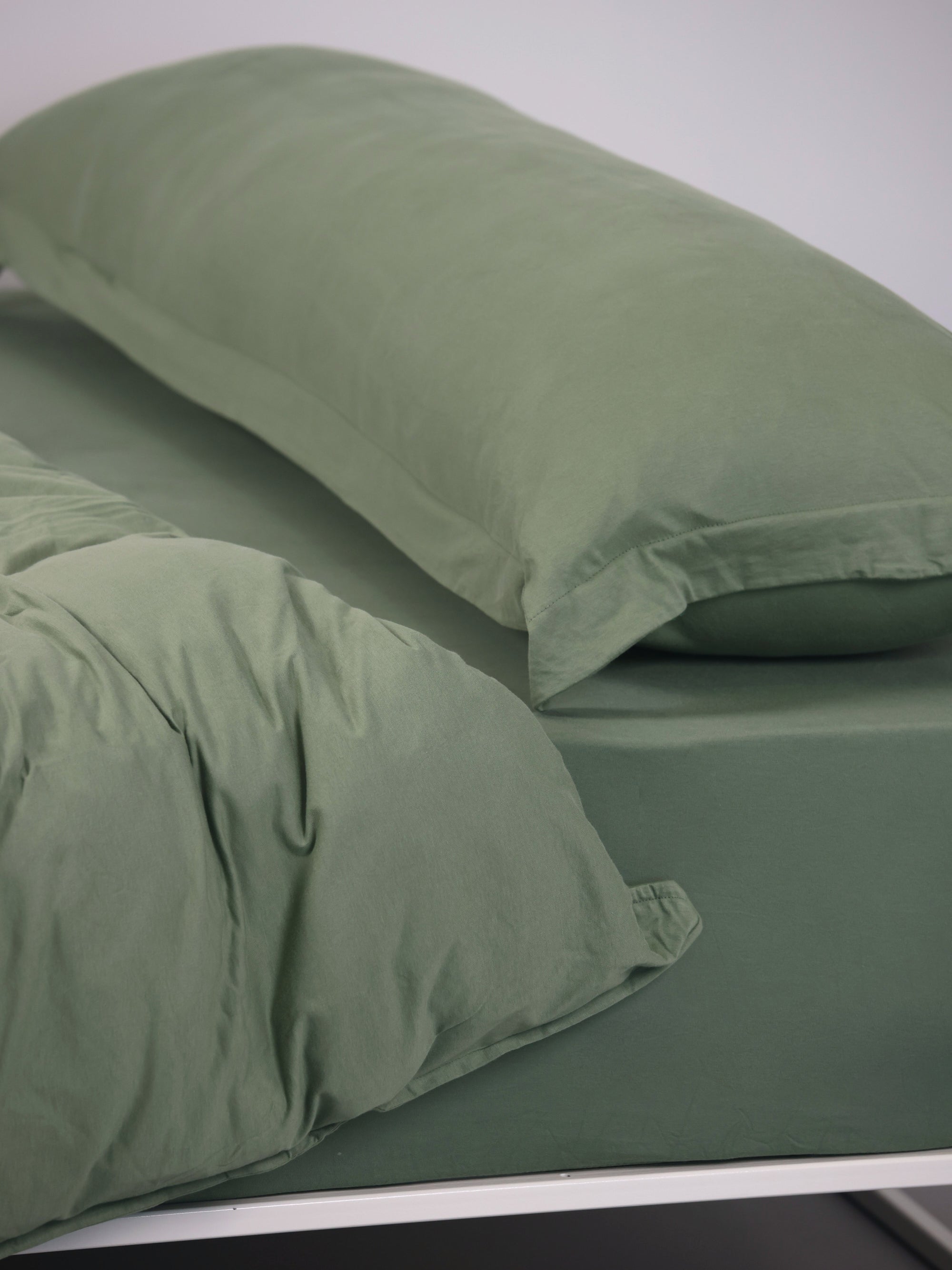 ראש מיטת ברזל לבנה עם סדין, שמיכת פוך, כרית וציפית לכרית ארוכה בצבע ערבה בחדר עם קירות אפורים