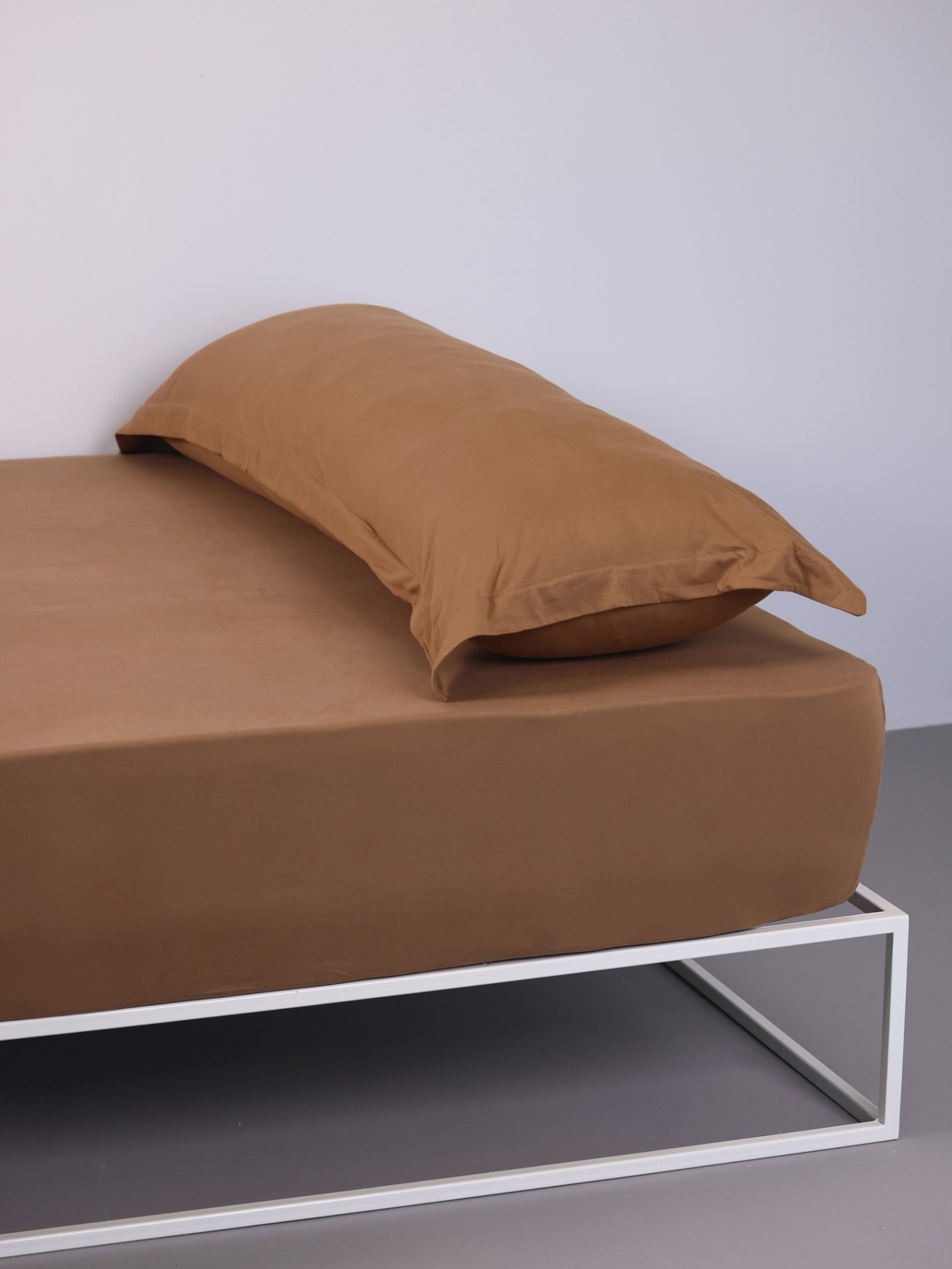 ראש מיטת ברזל לבנה עם סדין, כרית וציפית לכרית ארוכה בצבע טופי בחדר עם קירות אפורים