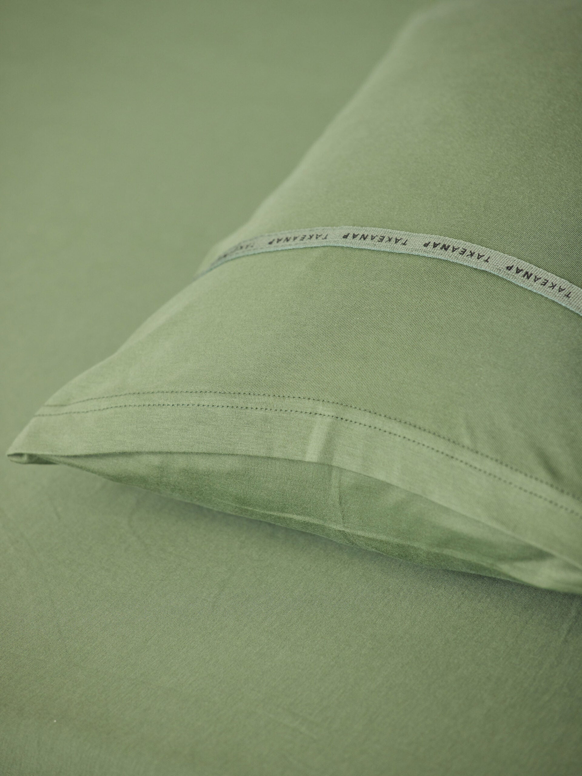 כרית עם ציפית על מיטת תינוק בצבע ירוק זית