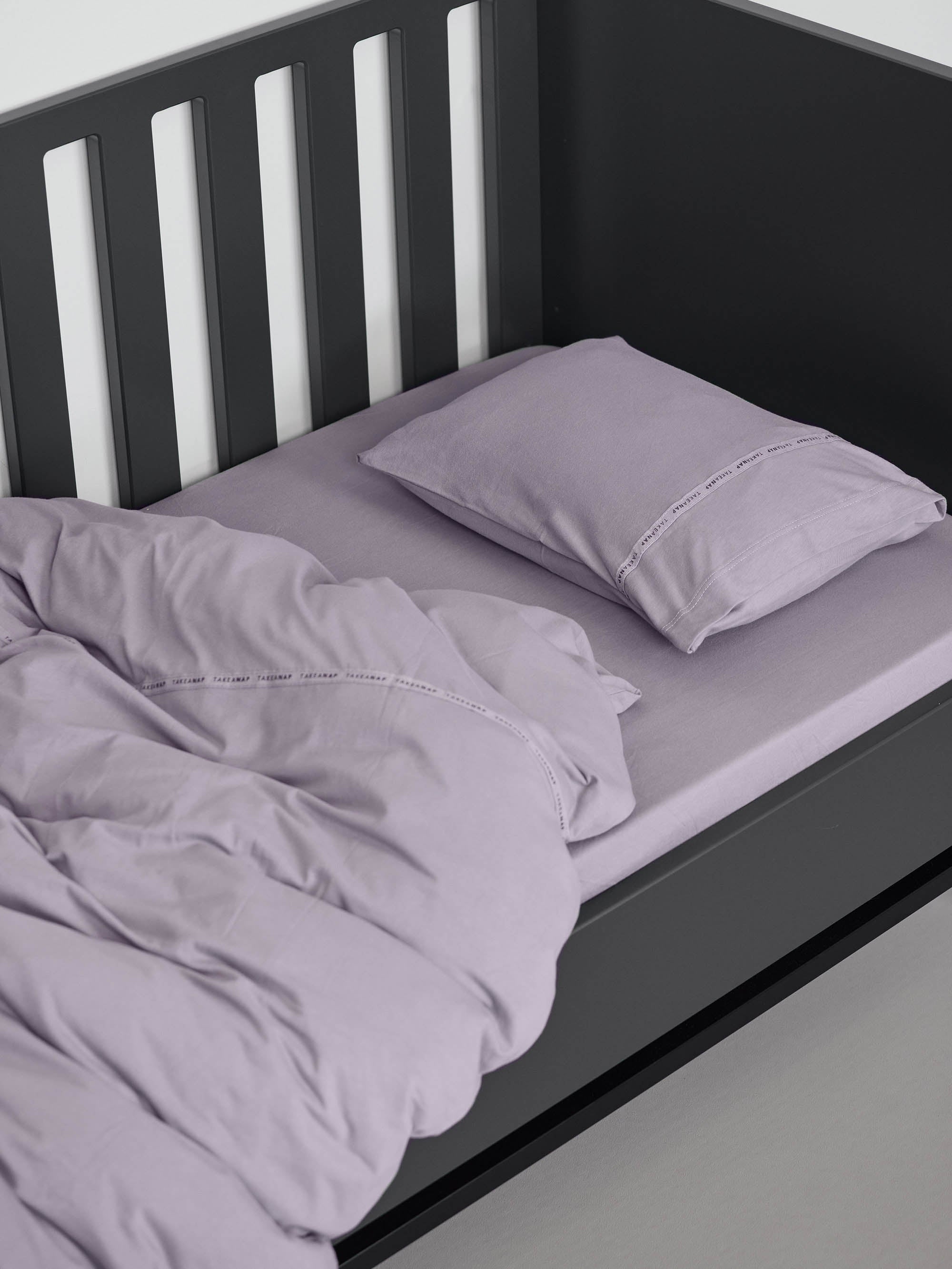 כרית עם ציפית לכרית קטנה בצבע סגול עם שמיכת פוך בתוך מיטת תינוק שחורה