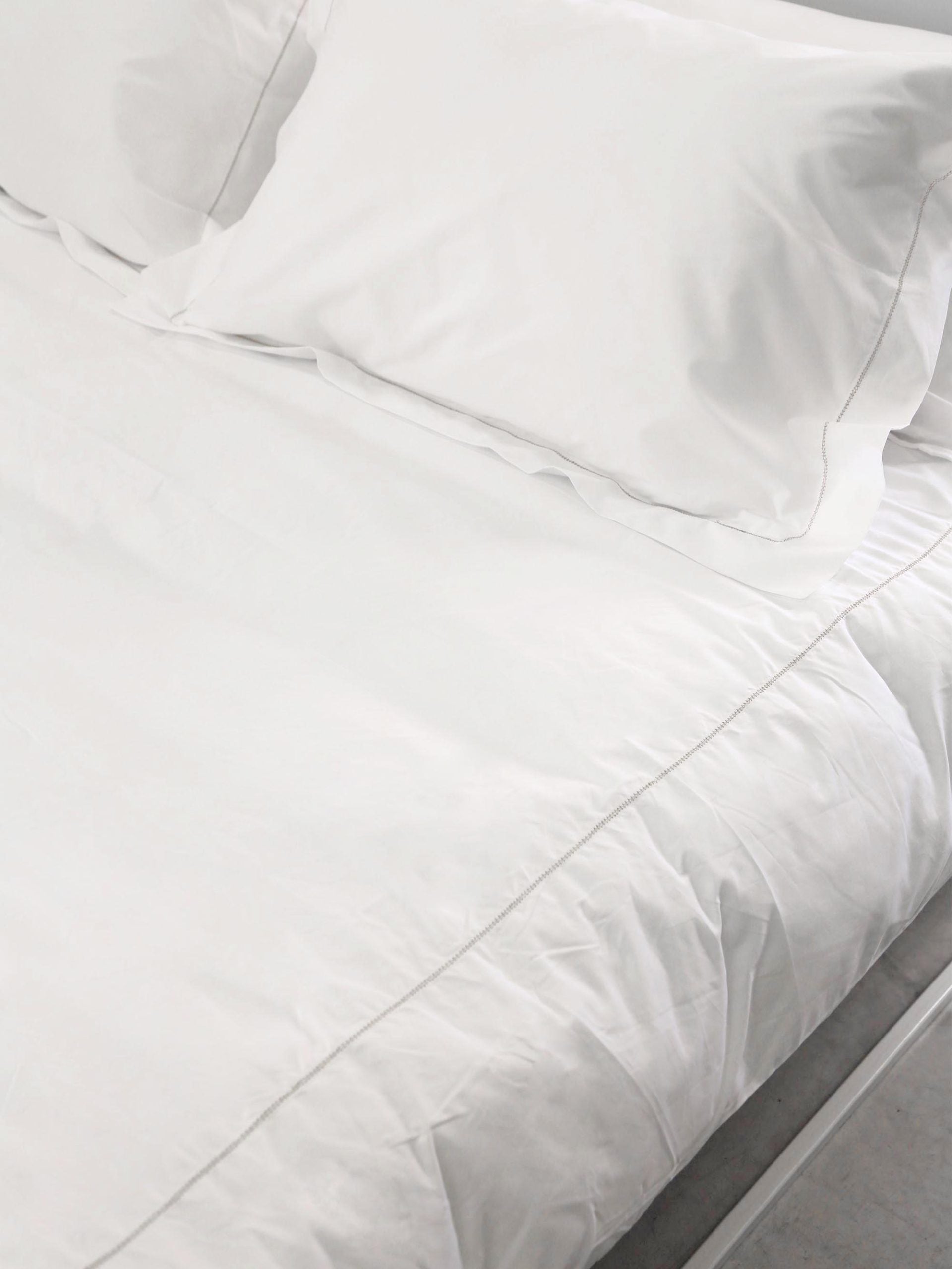 מצעים על מיטת ברזל לבנה הכוללים כריות עם ציפיות ושמיכה עם ציפה
