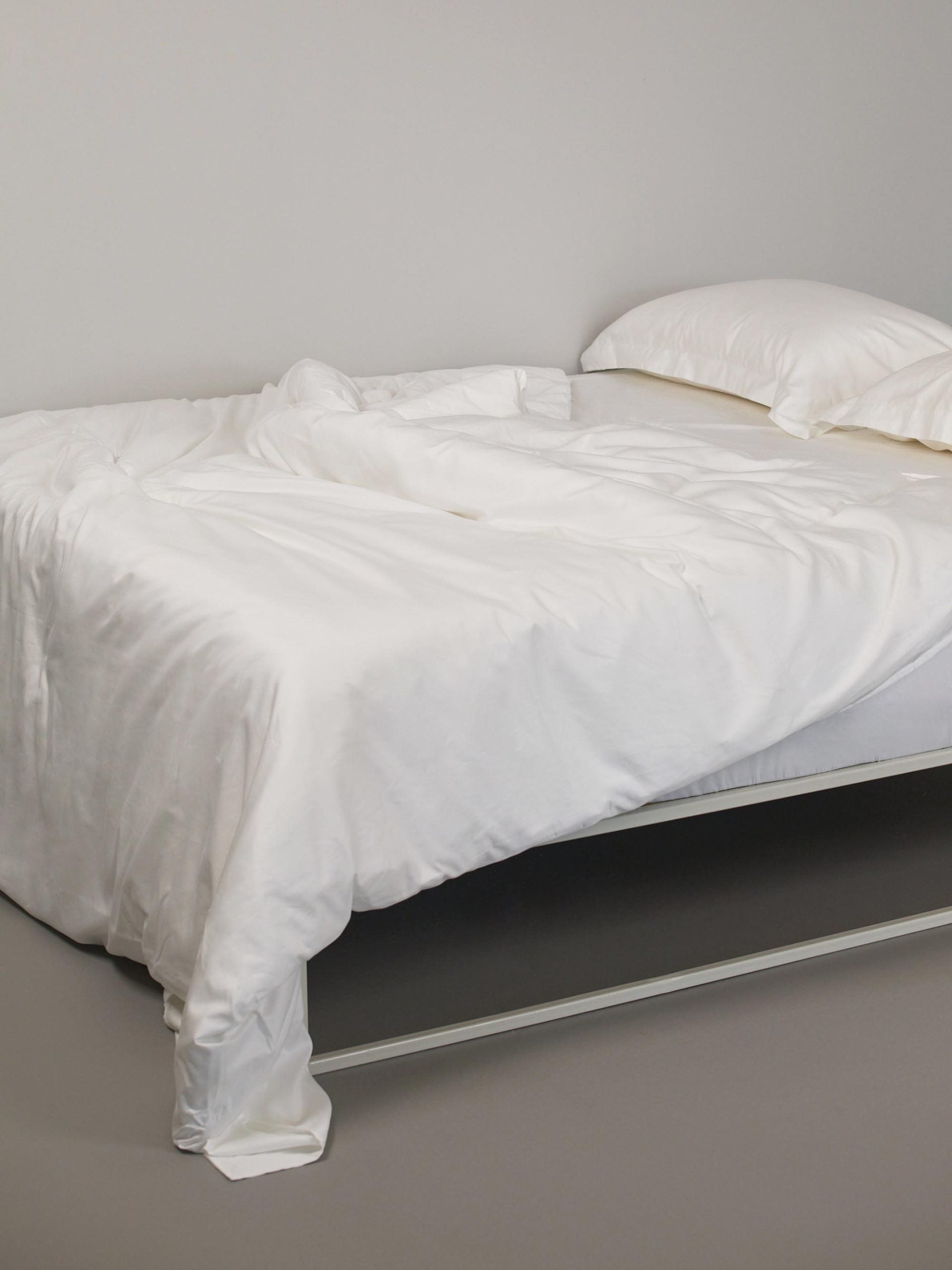 סדין זוגי מסאטן, שמיכת פוך וכרית ארוכה על מיטת ברזל לבנה
