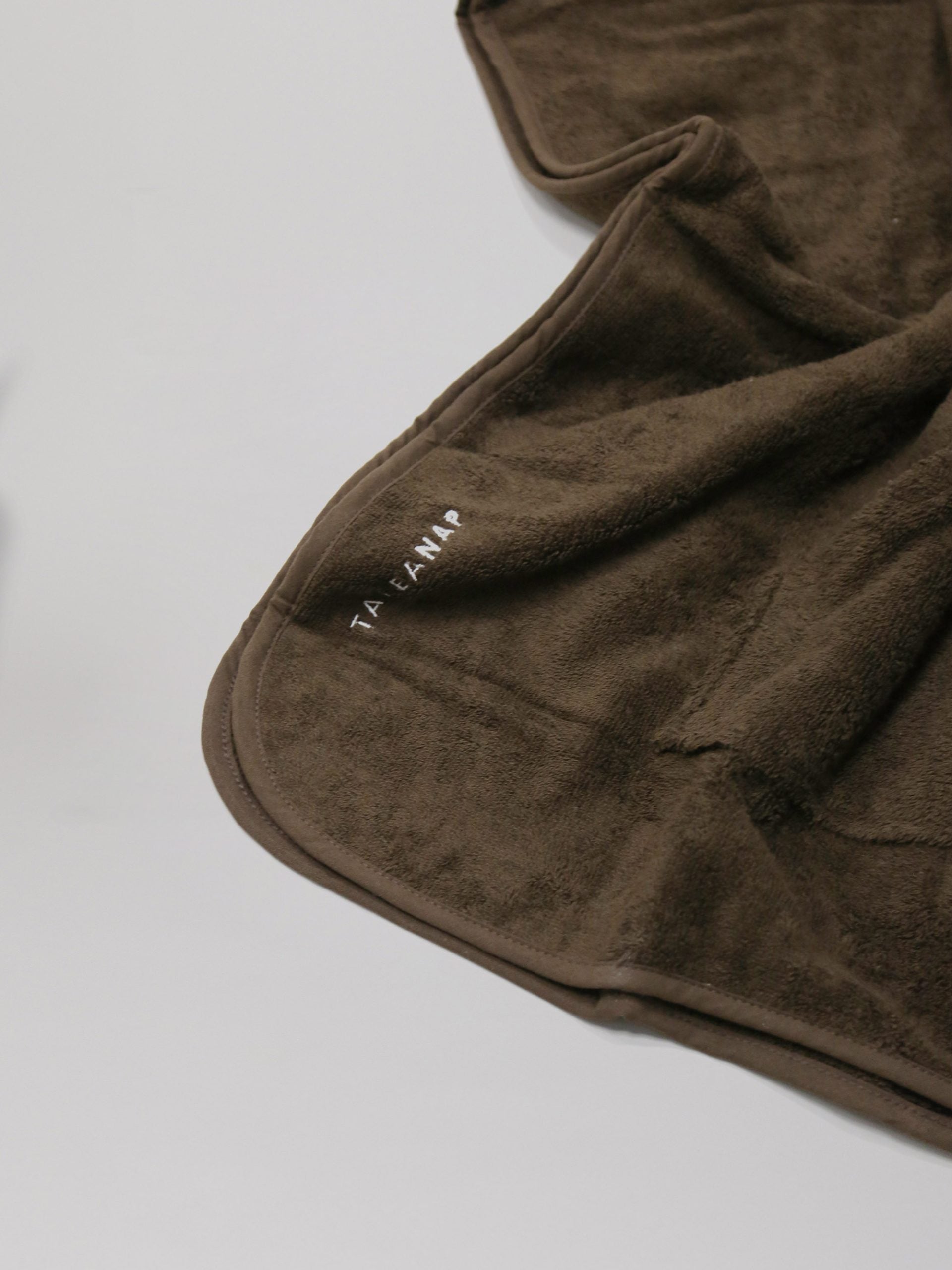 פינת מגבת פונצ'ו לילדים בצבע חום פרושה על רקע אפור