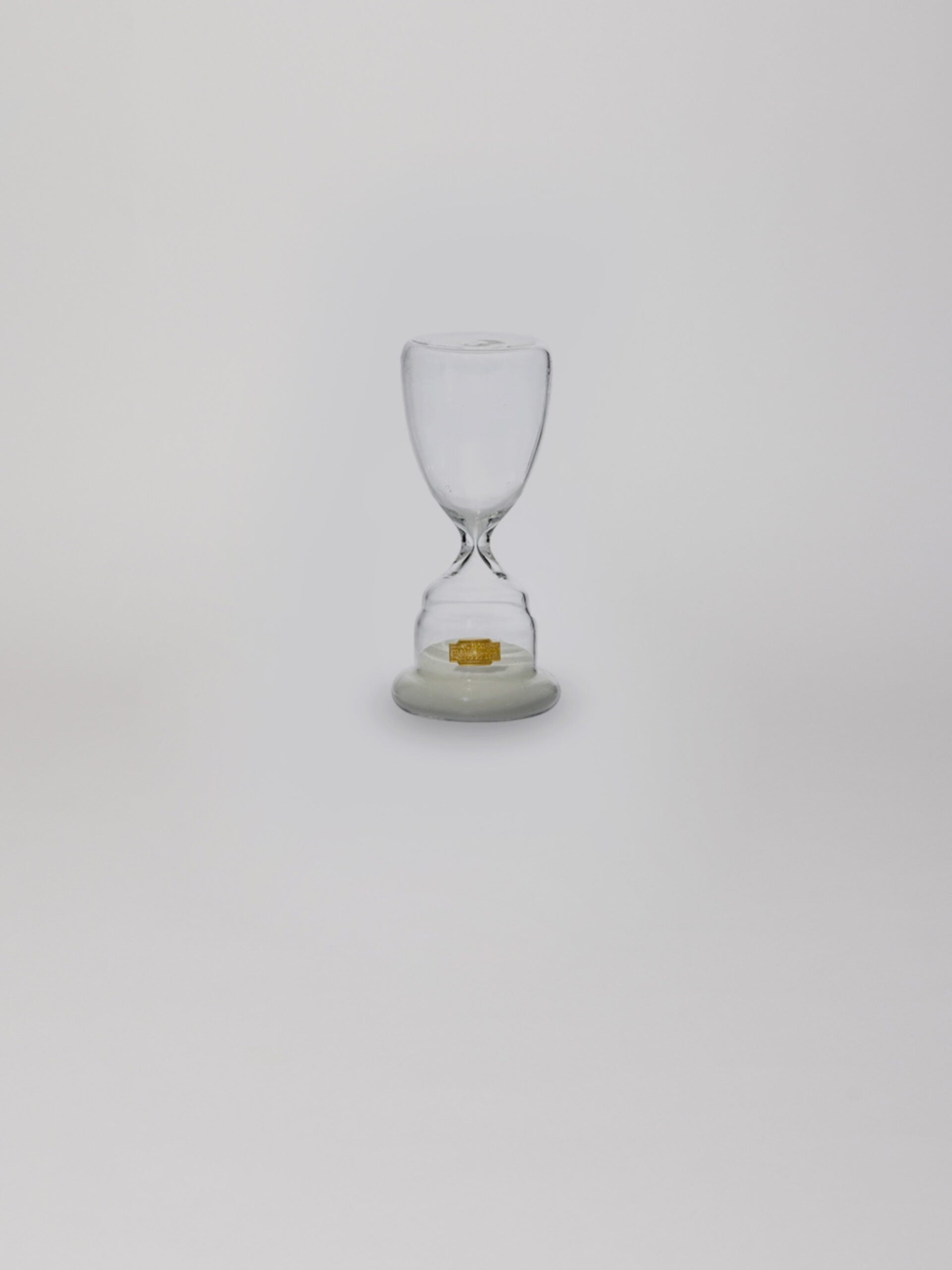 שעון חול מזכוכית בצבע לבן עם חול בחלקו התחתון על עומד על רקע אפור בהיר
