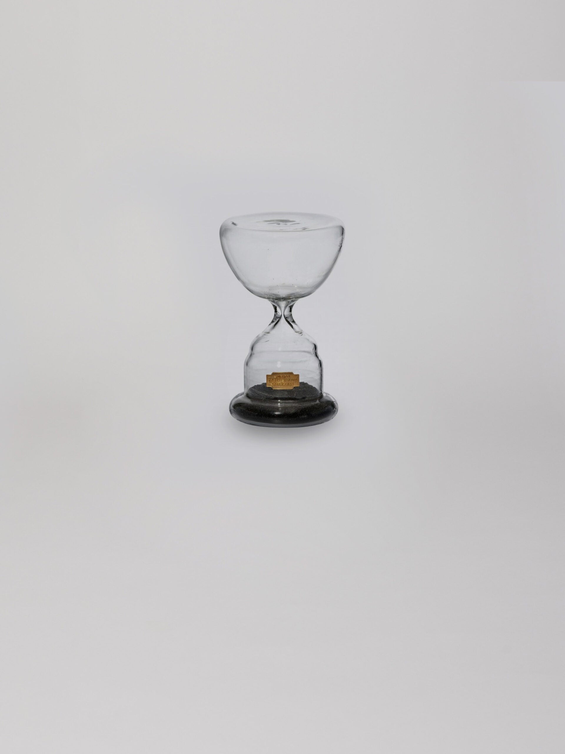 שעון חול מזכוכית בצבע שחור עם חול בחלקו התחתון על עומד על רקע אפור בהיר