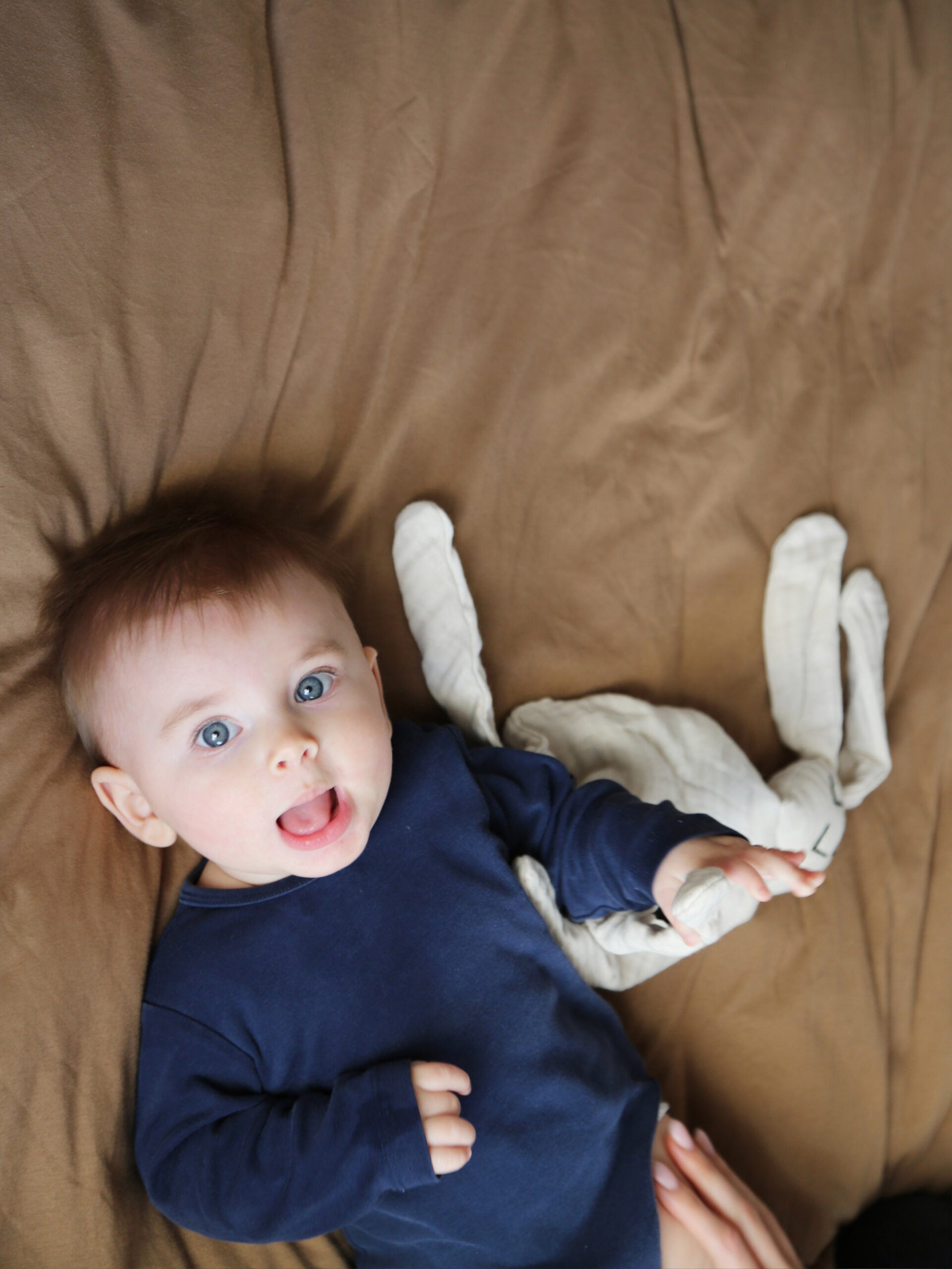 היי הגעתם לדף המוצר של חפץ מעבר נבי ארנבי Dream | בתמונה: תינוק בלונדיני עם עיניים כחולות שוכב על המיטה ומחזיק חפץ מעבר לבן
