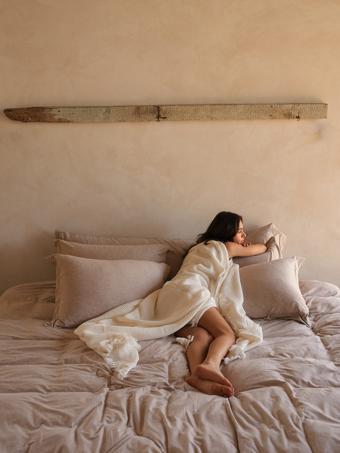 אישה מכוסה בשמיכה נשענת על סט כריות על מיטה עם סט מצעים איכותיים