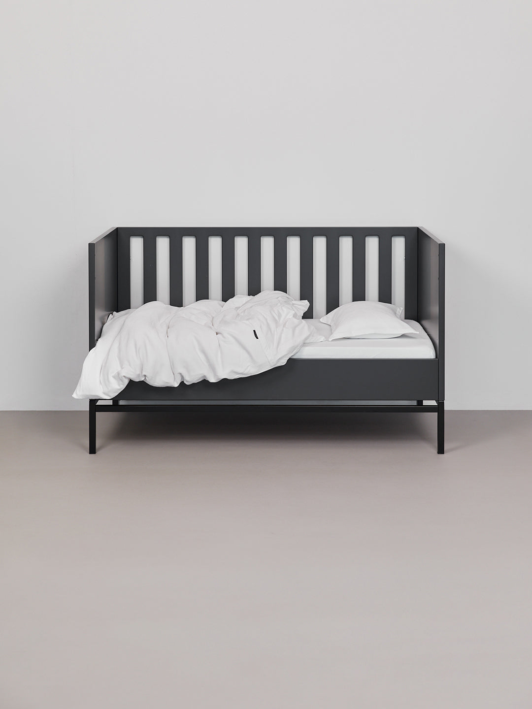 מצעים למיטת תינוק בצבע לבן בתוך עריסה שחורה פתוחה הכולל סדין, שמיכת קיץ וכרית
