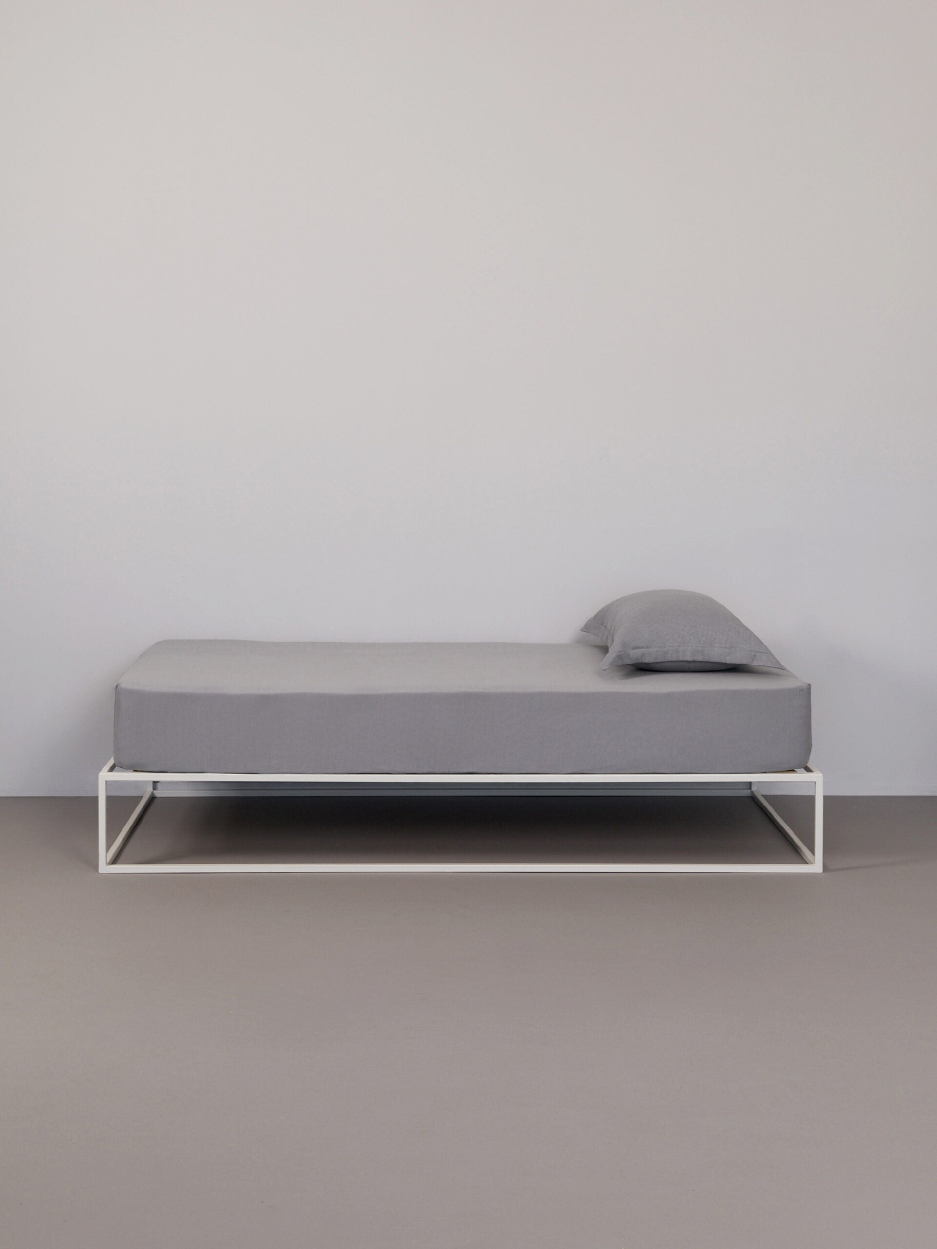 בתמונה: מיטת ברזל לבנה עם סדין וכרית עם ציפית לכרית טריקו Jacquard בצבע אפור