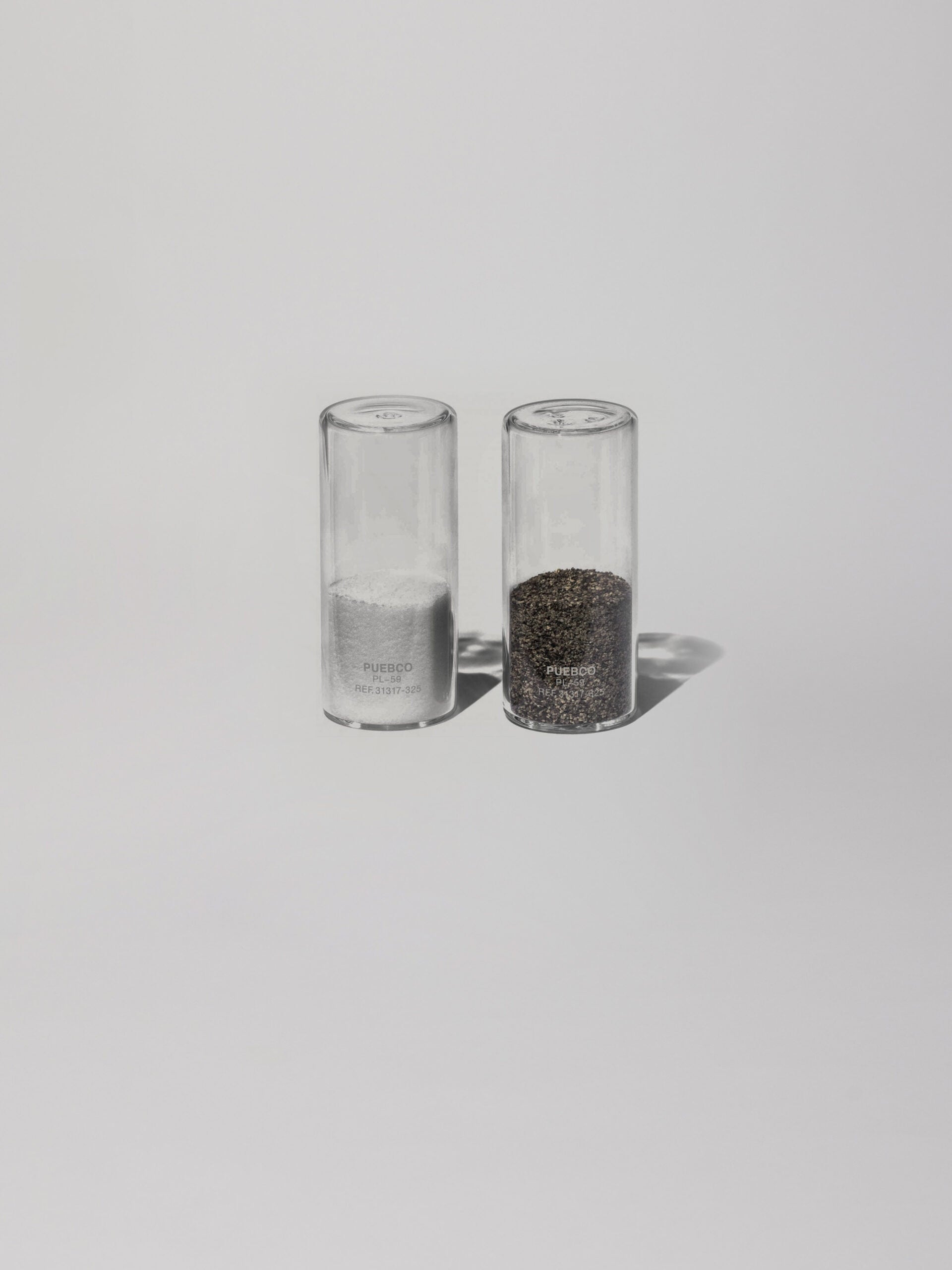 מלחיה ופלפליה רבע מלאים עשוי זכוכית עומדים על רקע אפור בהיר 